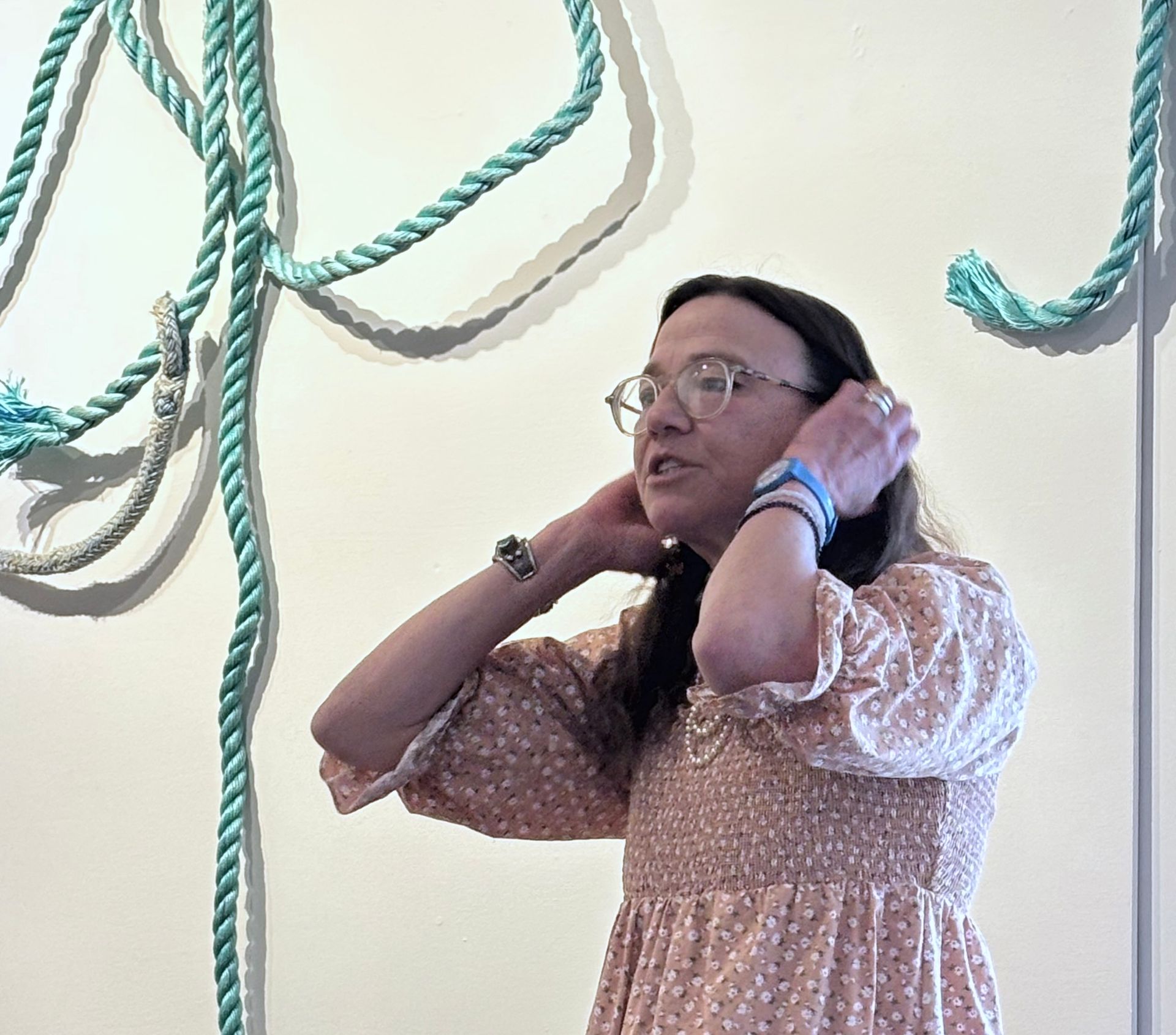 Woman adjusting her hair beside teal rope decor on a white wall