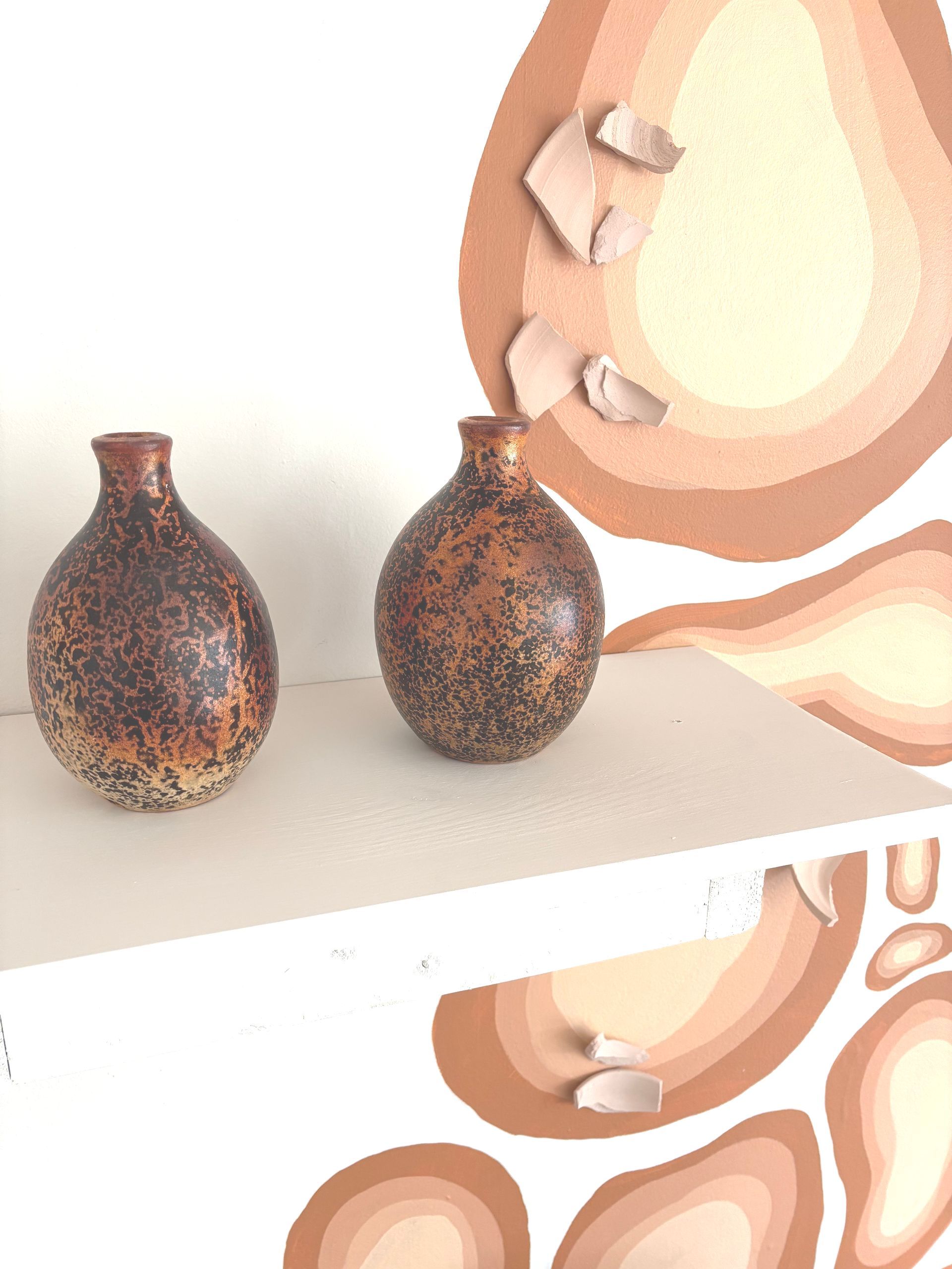 Two speckled brown vases on a white shelf beside a framed abstract peach-and-beige artwork.