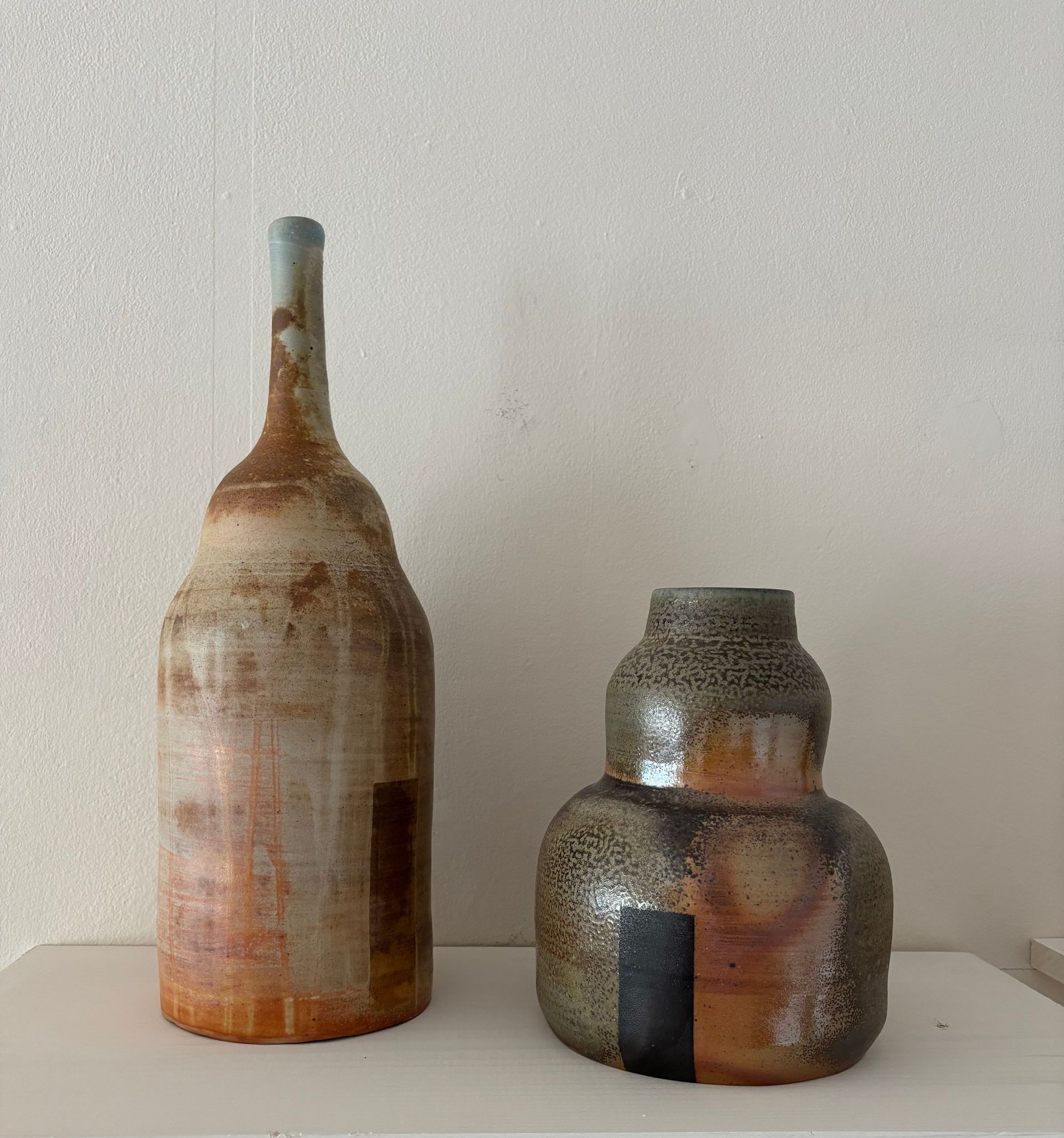Two rustic ceramic vases on a white shelf against a plain wall.