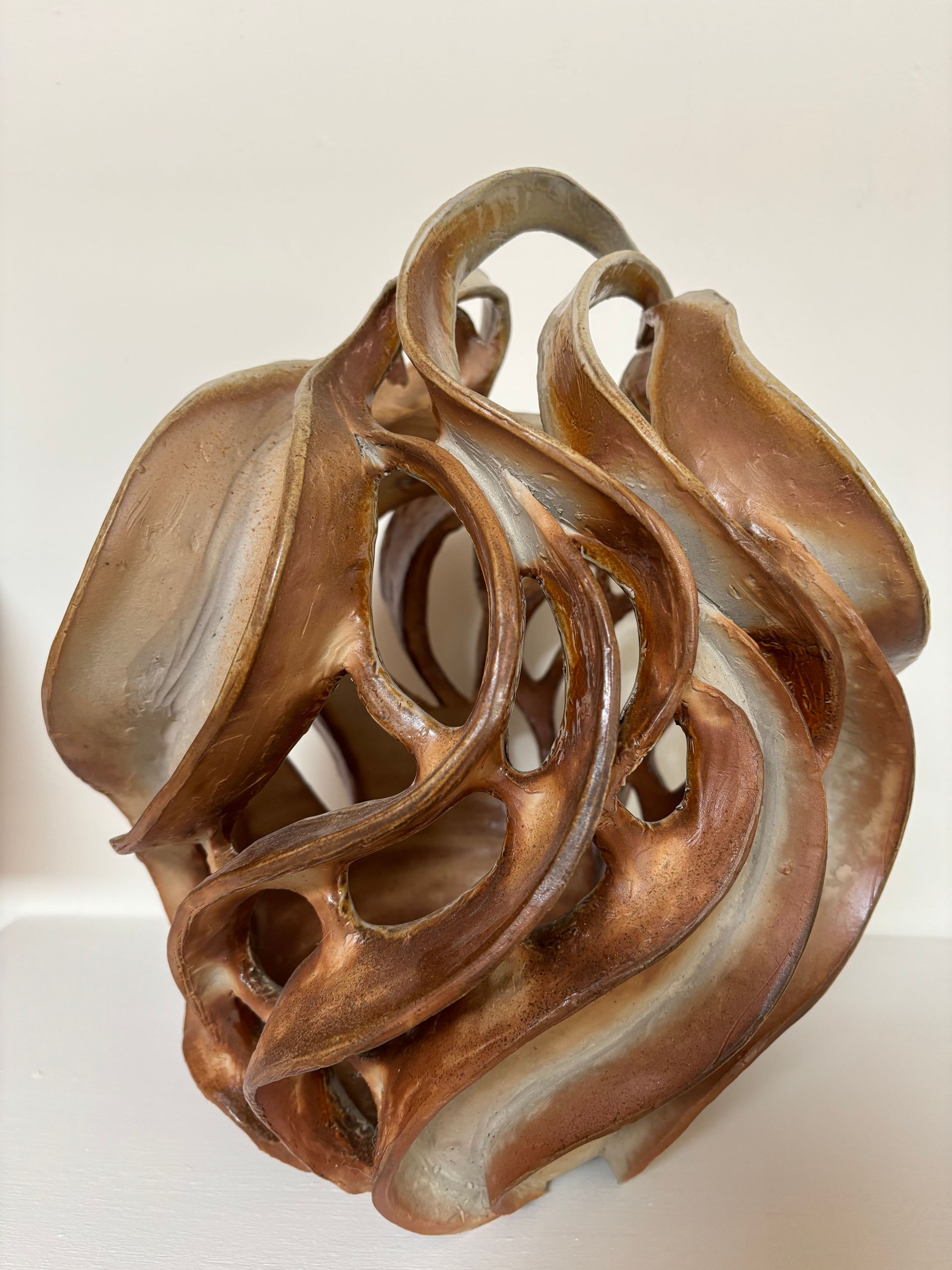 Abstract bronze and silver-toned sculptural form with flowing, intertwined curves on a light background