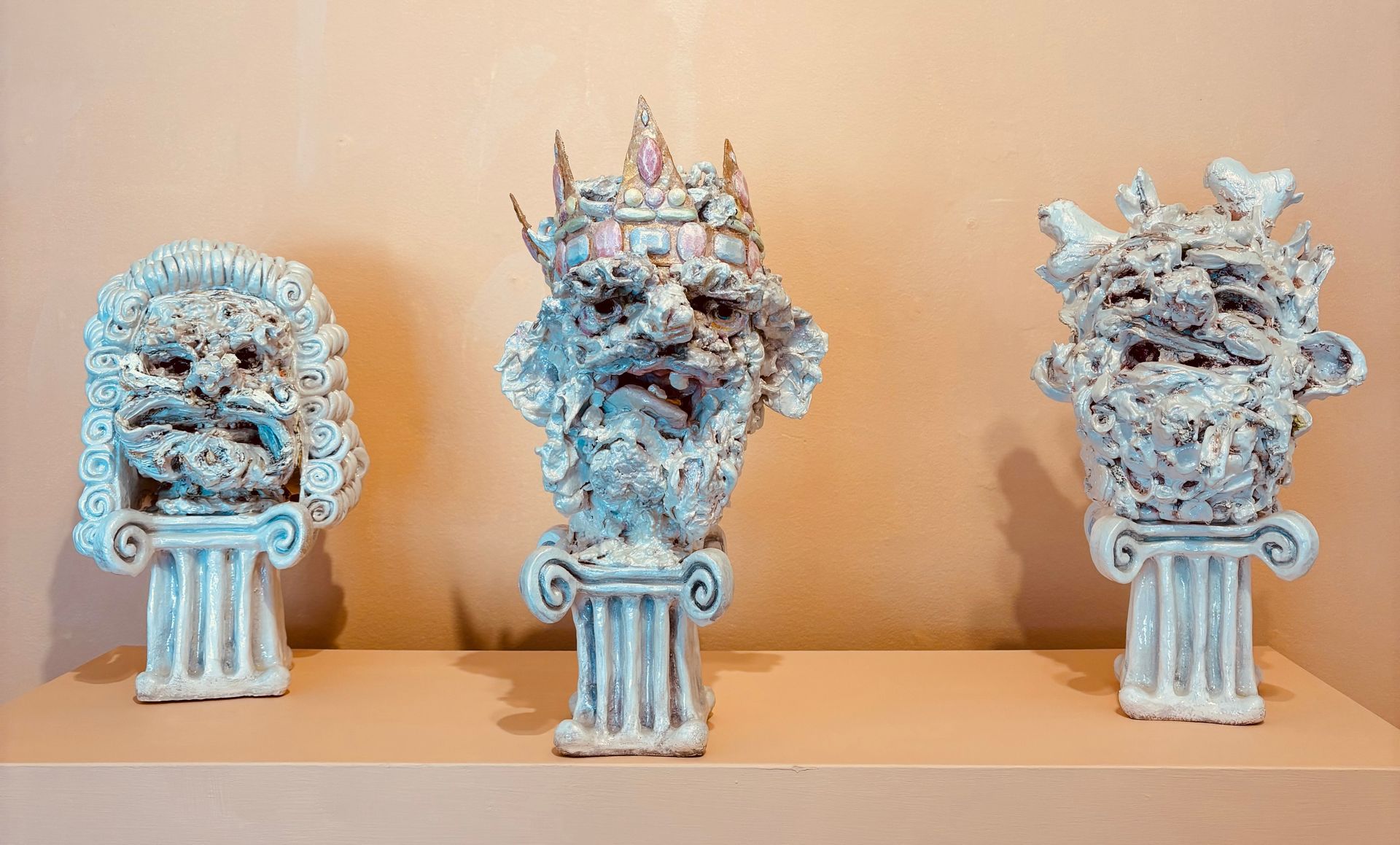 Three blue-white ornate bust sculptures on white pedestals against a tan wall.
