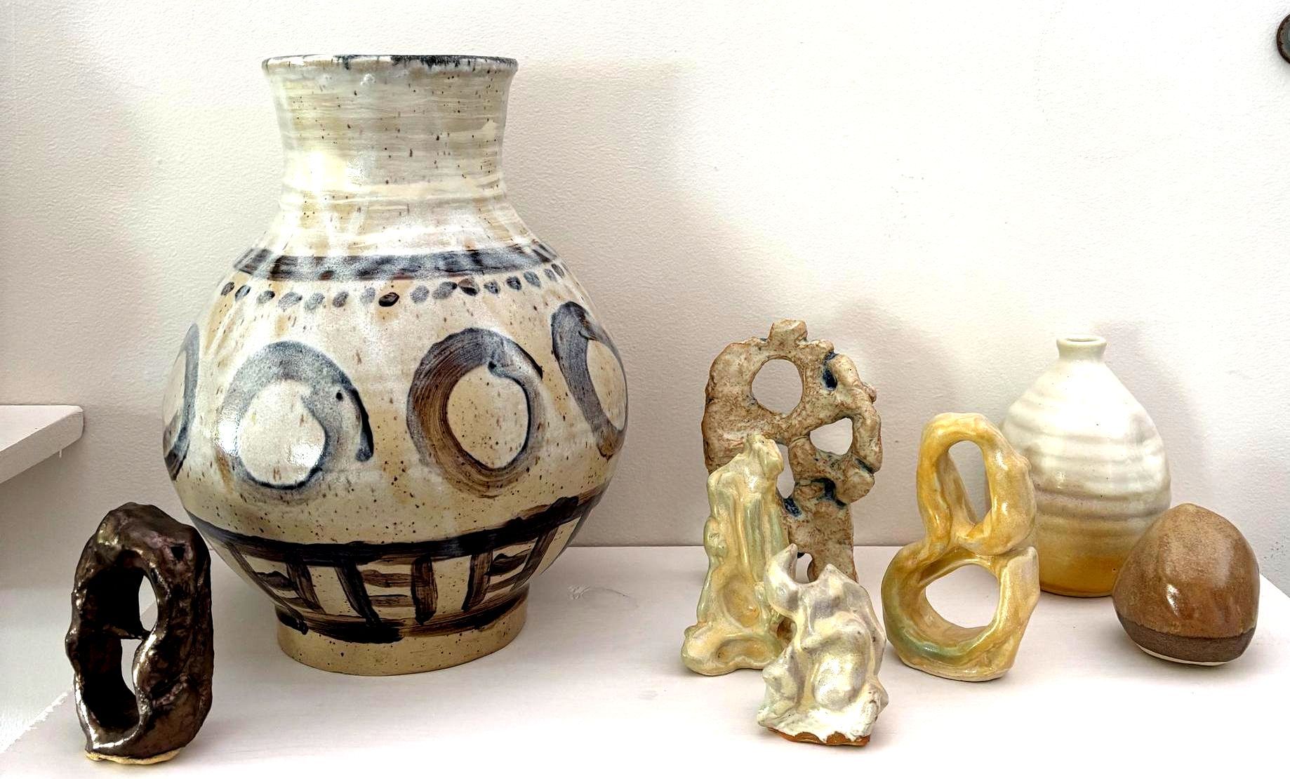 Assorted small ceramic and stone vessels and figurines displayed on a white surface against a wall