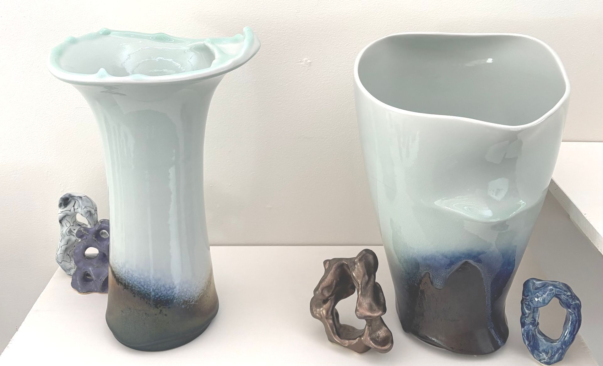 Two pale blue ceramic vases with shell and stone accents on a white background