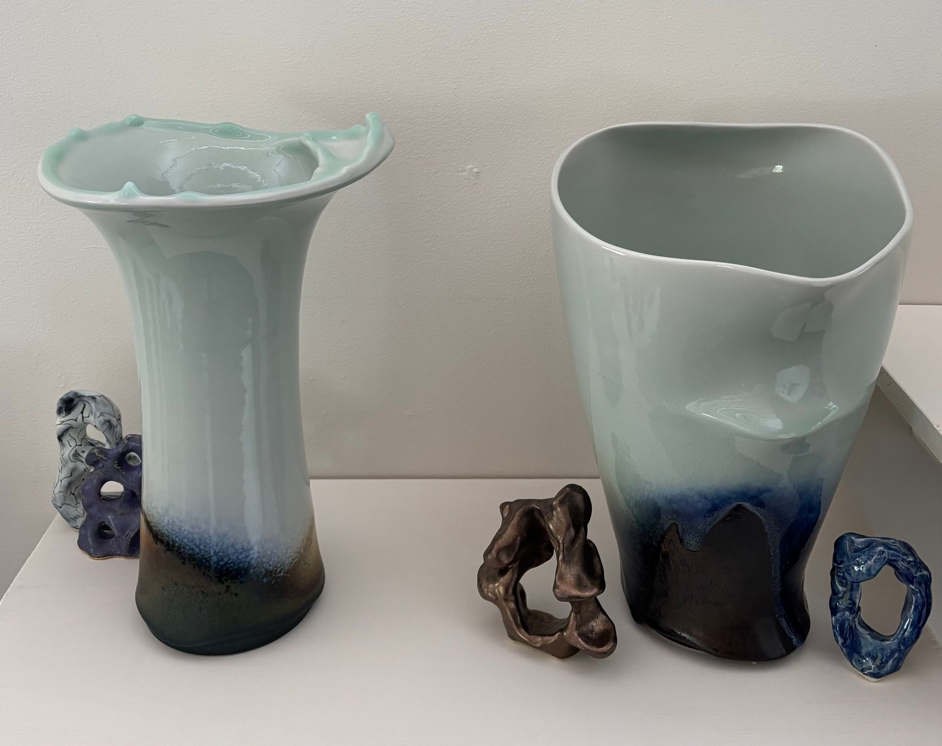 Two white-blue ceramic vases with irregular rims, flanked by small decorative figurines on a plain background.