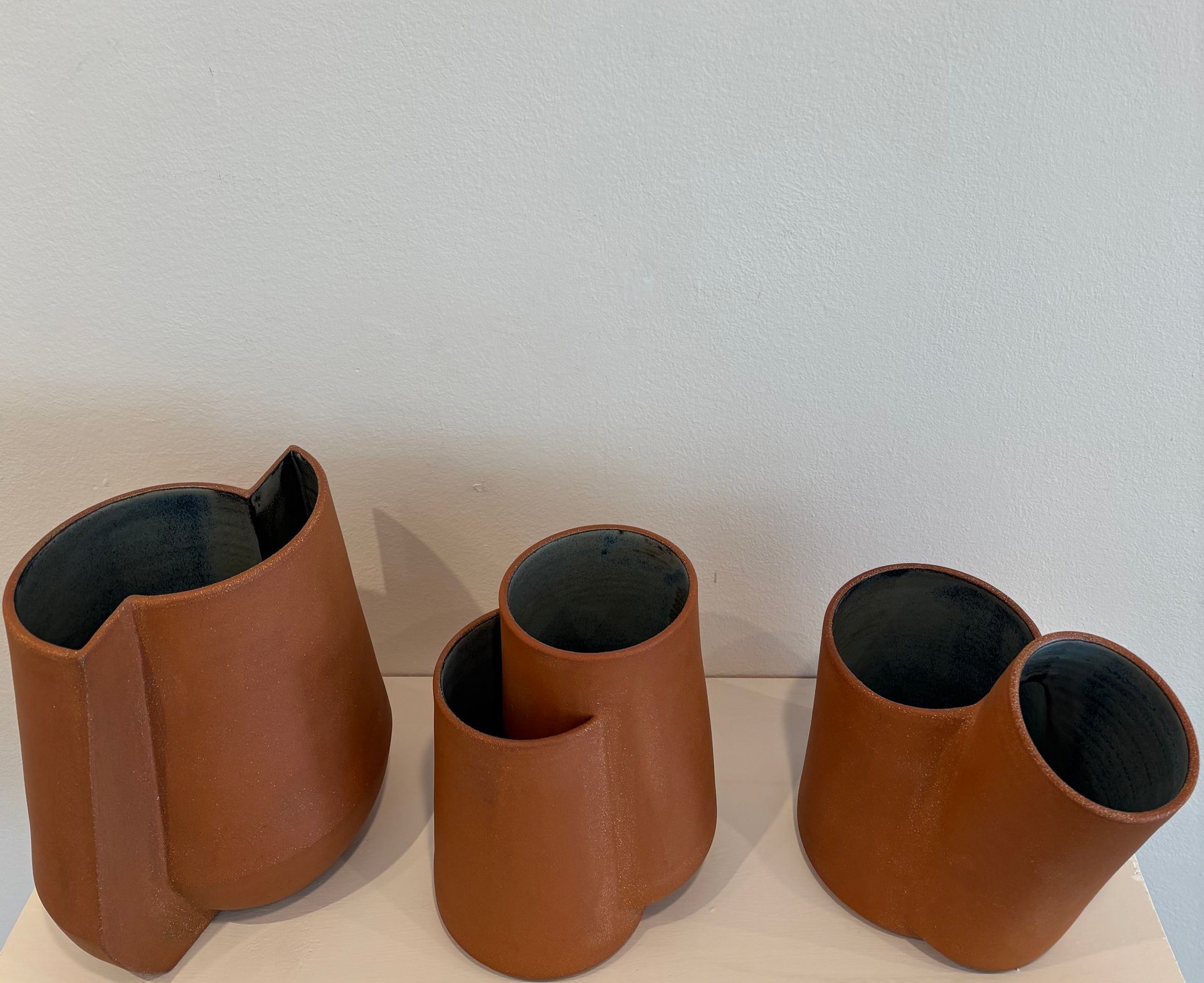 Three brown leather storage bins with dark interiors arranged on a shelf against a light wall