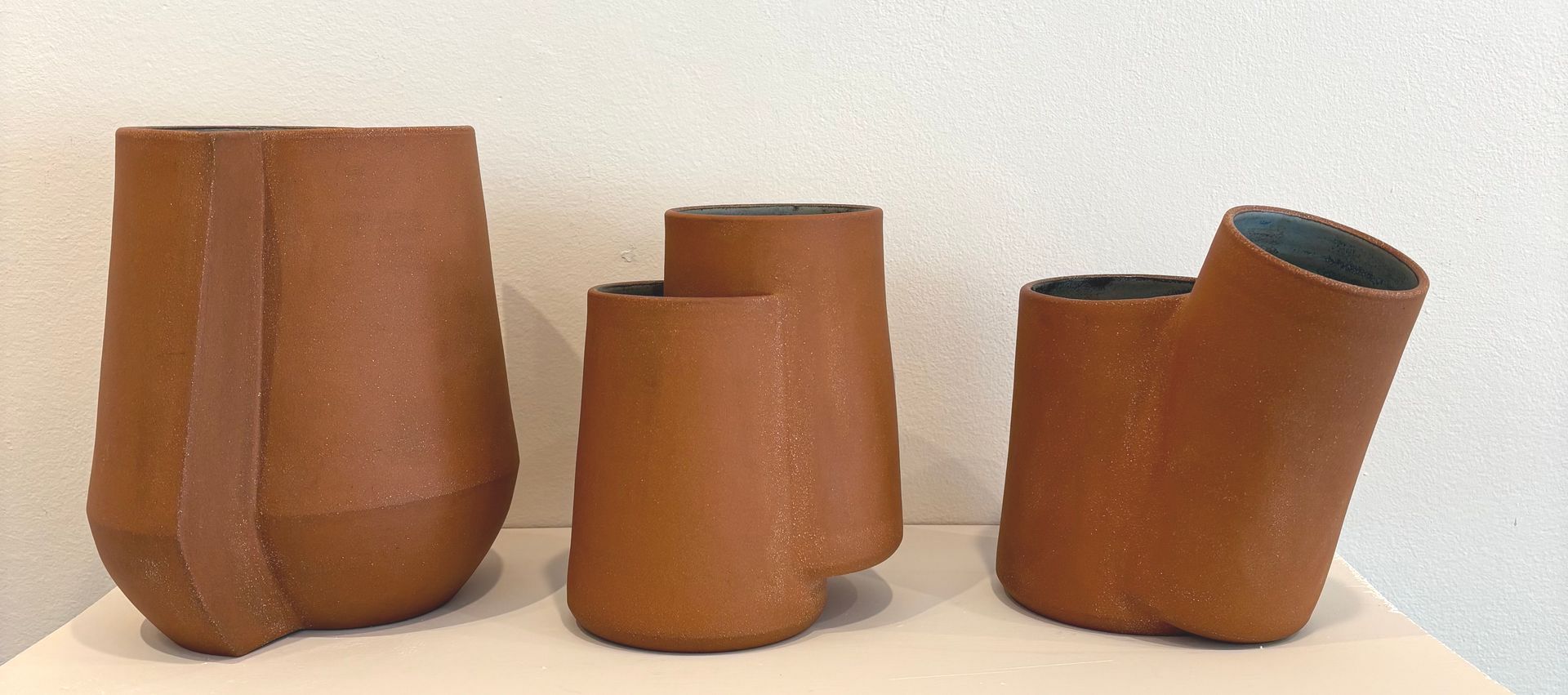 Four brown ceramic pots of varying sizes and shapes on a white surface against a light wall