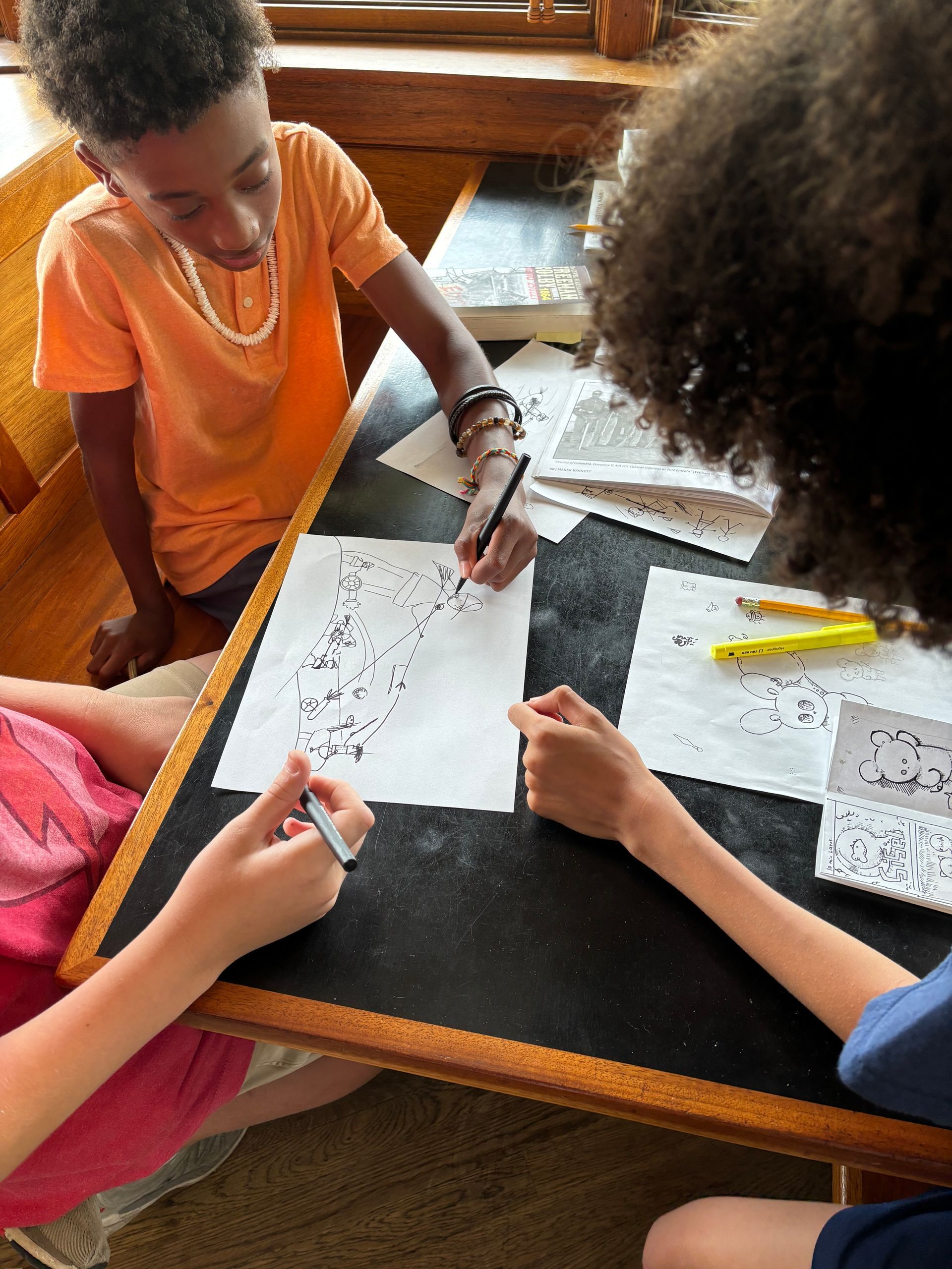 Three people collaborate at a table, pointing and writing on printed worksheets.