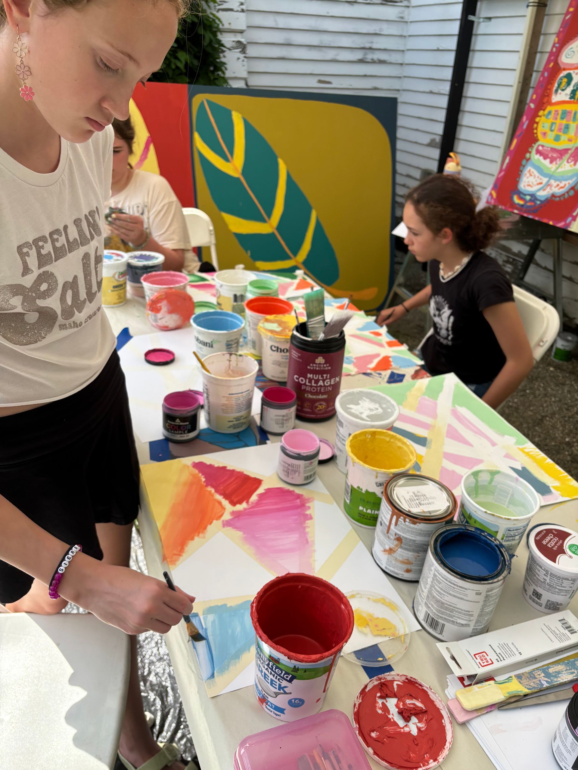 People painting at a table with colorful art supplies and abstract leaf designs