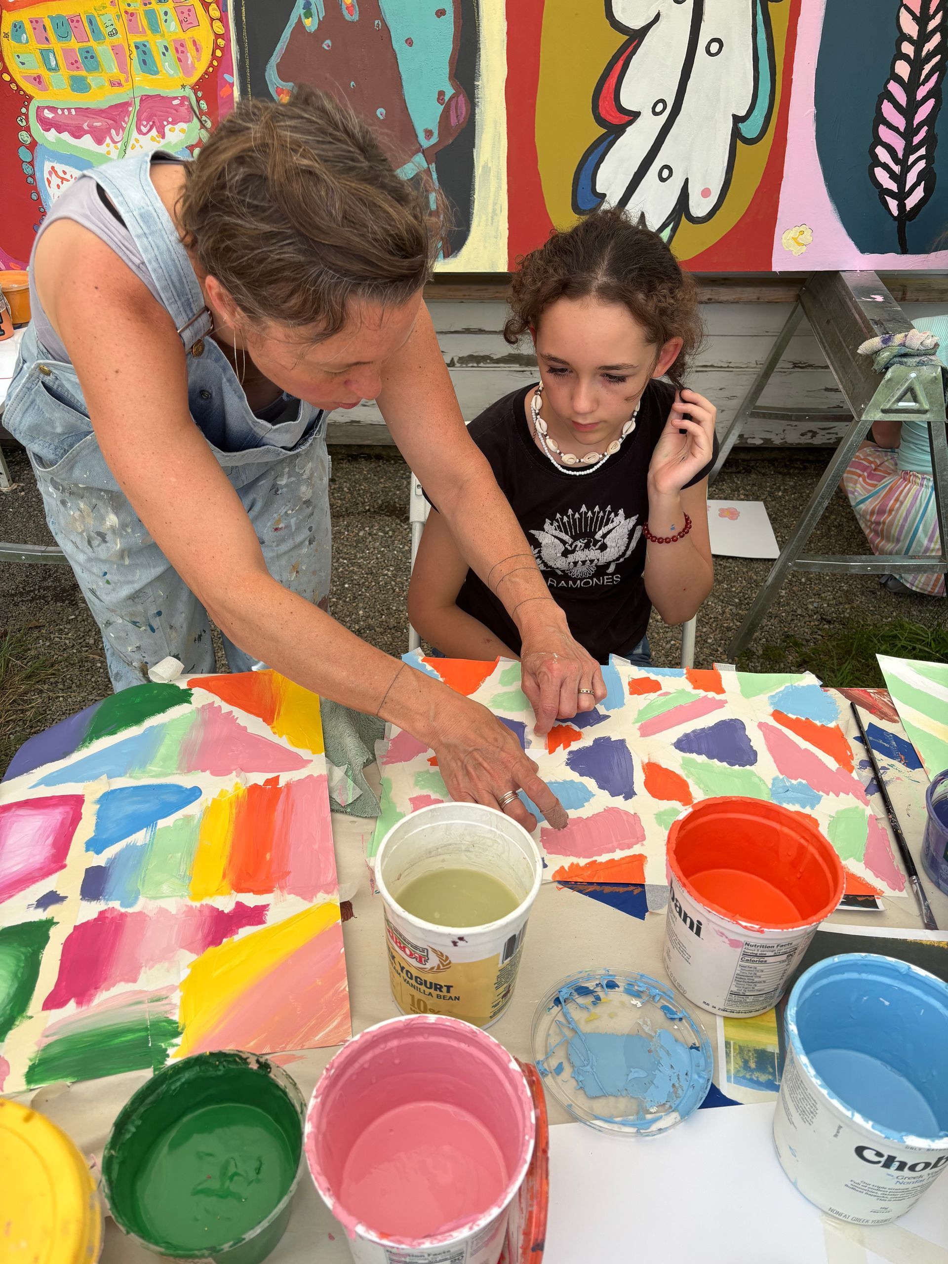 Two children painting a colorful mural at a table with paint cups.