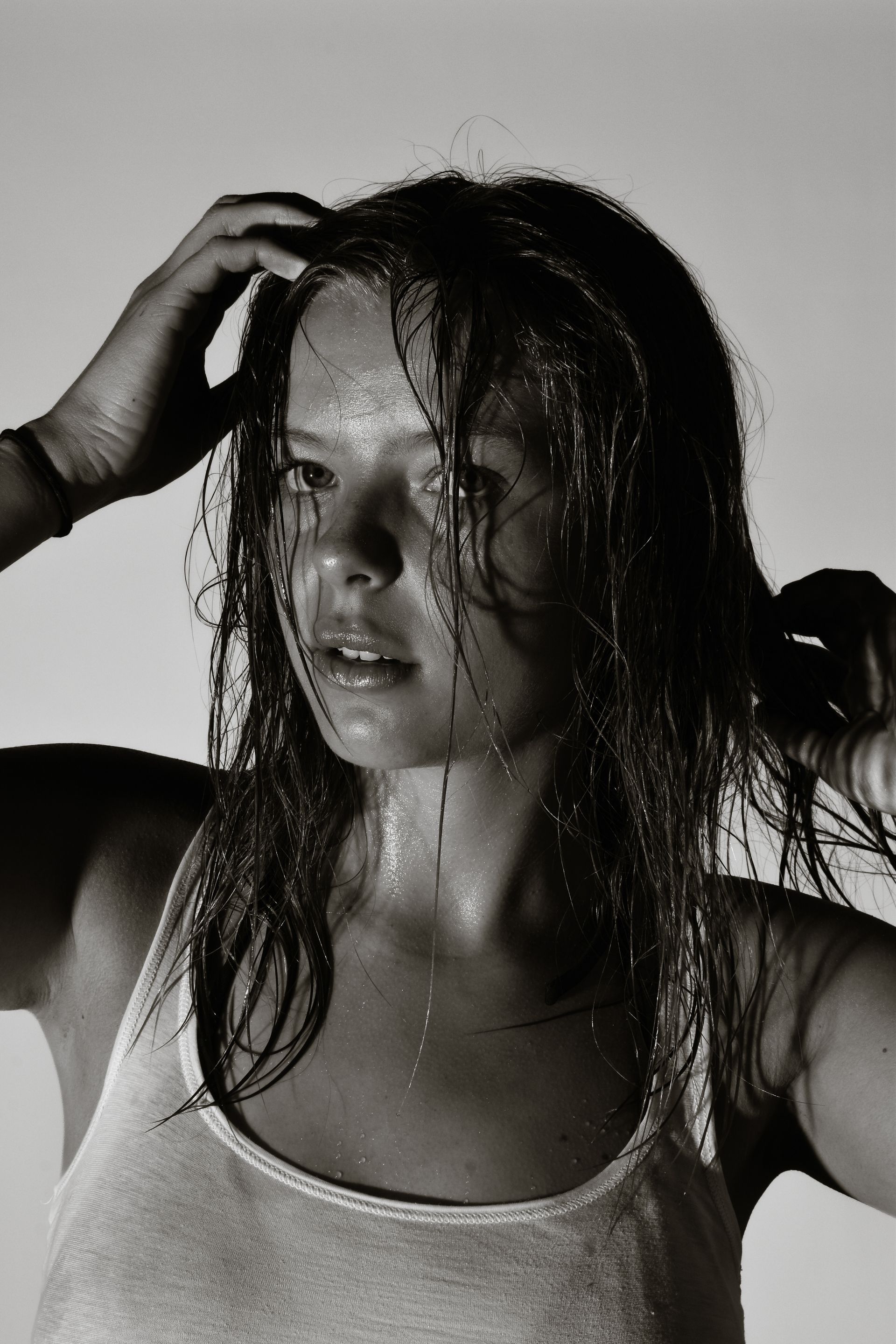 Black-and-white portrait of a wet-haired woman touching her head against a plain background