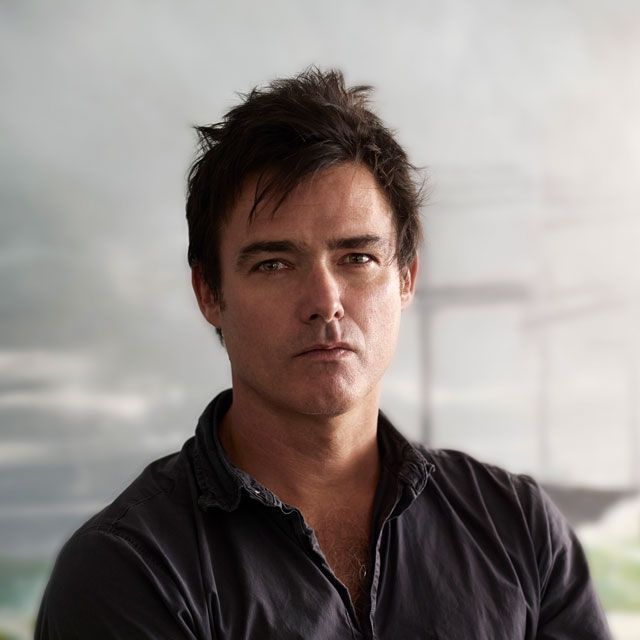 Portrait of a man in a dark shirt against a blurred gray outdoor background