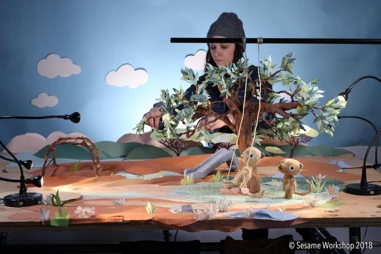 Person in a beanie arranging leafy branches and toy animals on a tabletop landscape stage