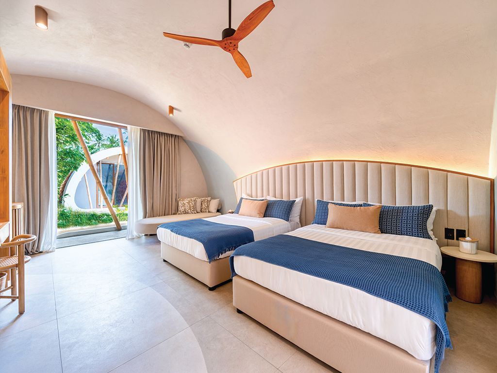Bright modern bedroom with two blue beds, wood ceiling fan, and sliding doors to a tropical view