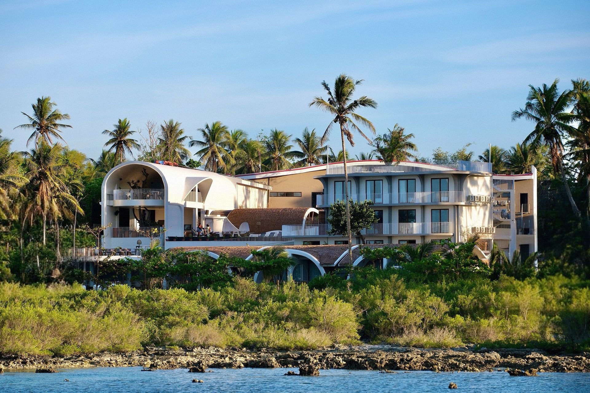 Modern beachfront villa with palm trees and greenery by the water