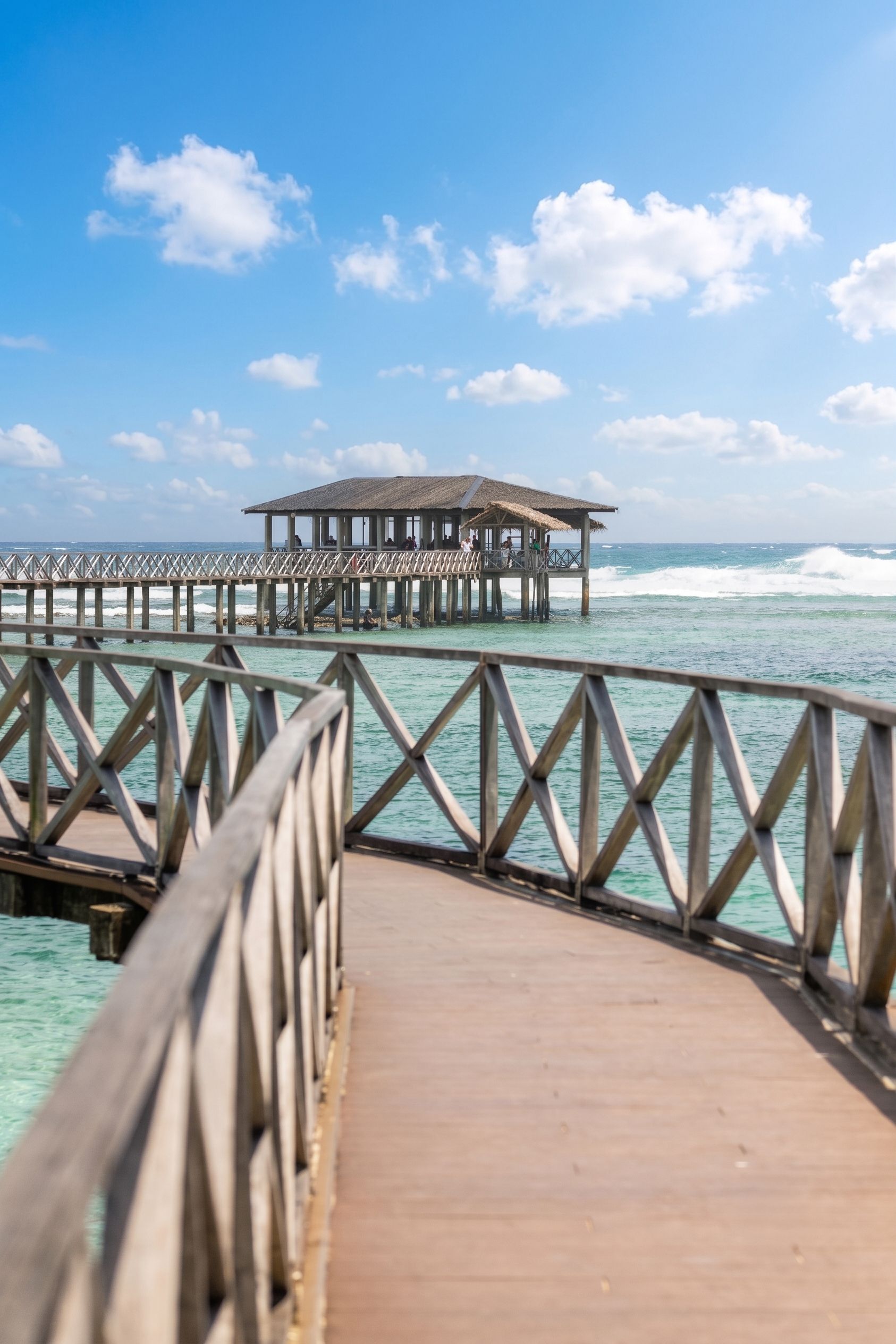 Wooden boardwalk leading to an ocean pier under a blue sky with clouds