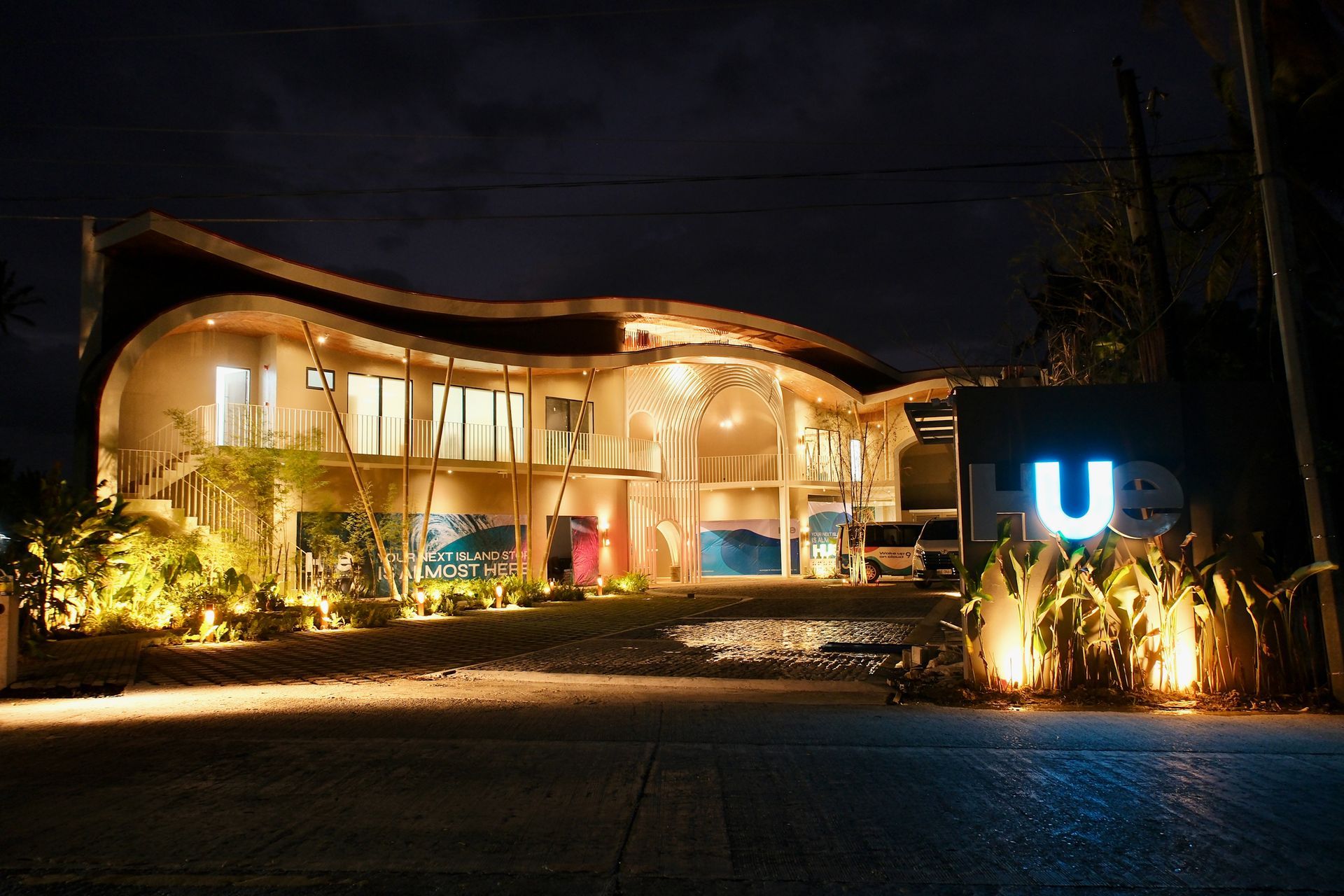 Modern building lit warmly at night with a glowing blue “U” sign by the entrance
