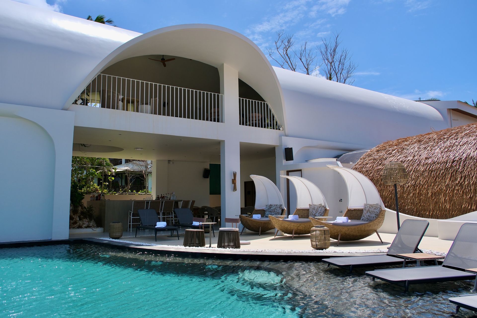 Modern white villa with curved balconies, a pool, and lounge chairs under a clear blue sky