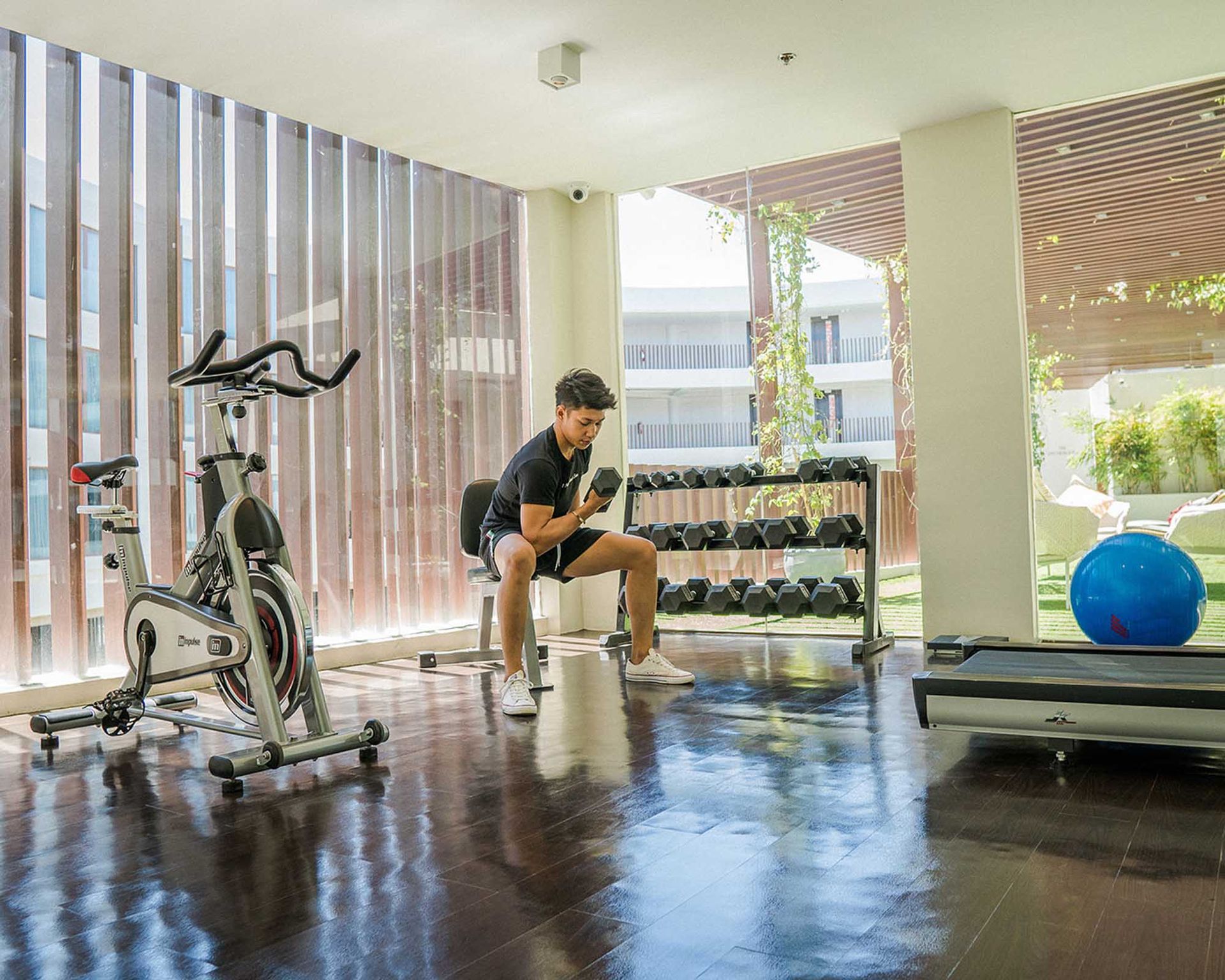 A man is sitting on a bench in a gym looking at his phone.