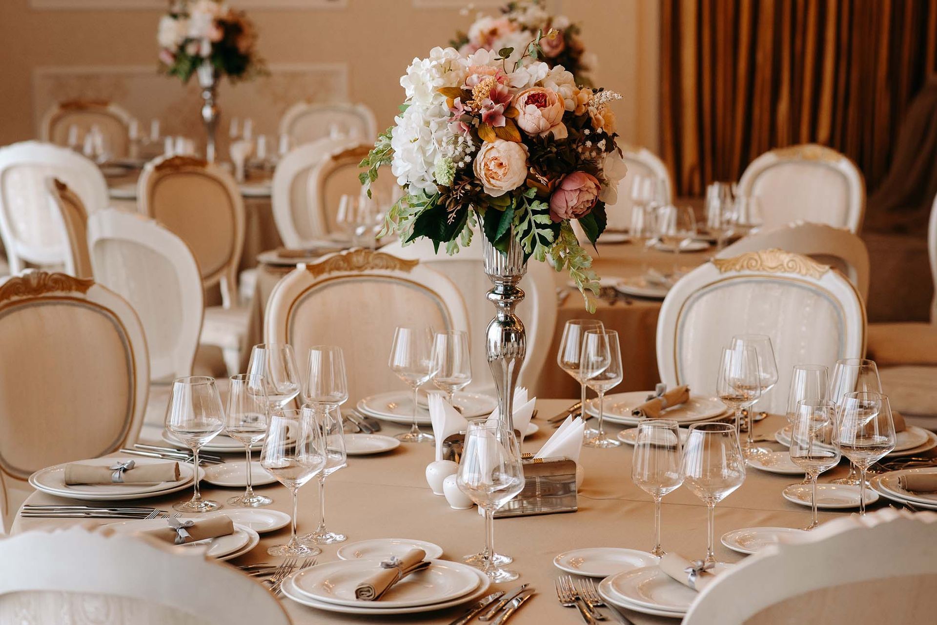 Elegant wedding reception tables with gold chairs, glassware, and floral centerpieces in a softly lit room