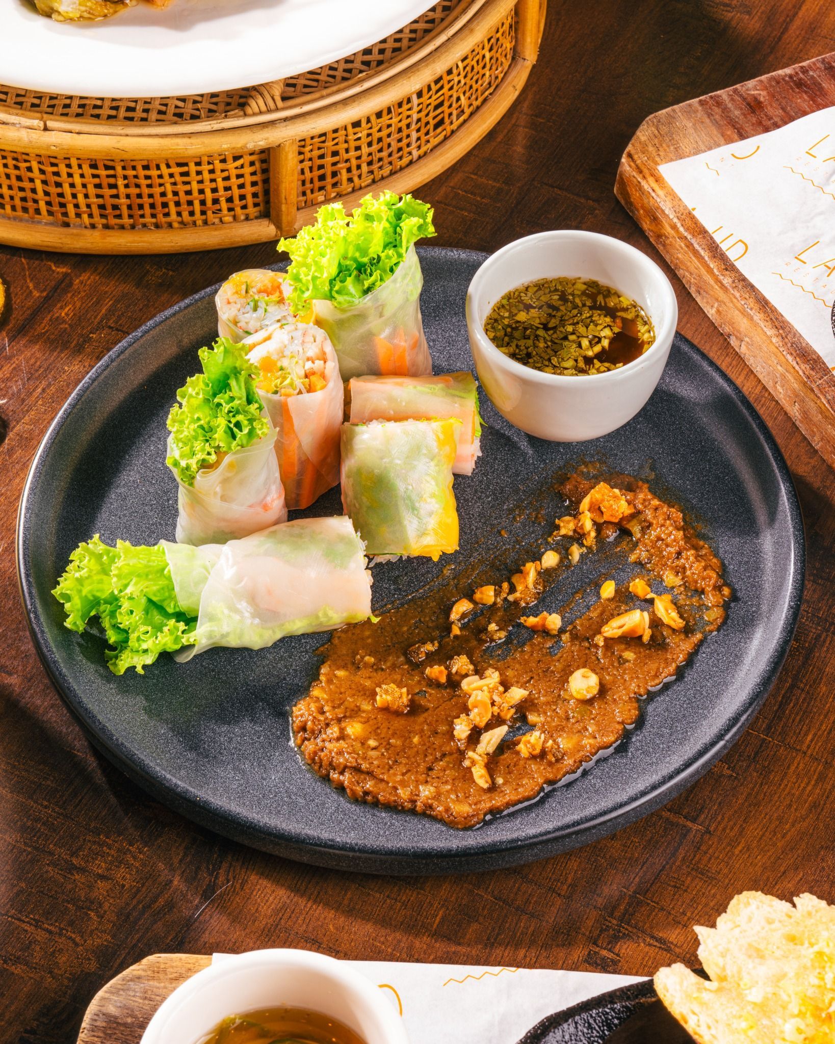 Sushi and a crisp brown appetizer on a black plate with dipping sauce on a wooden table