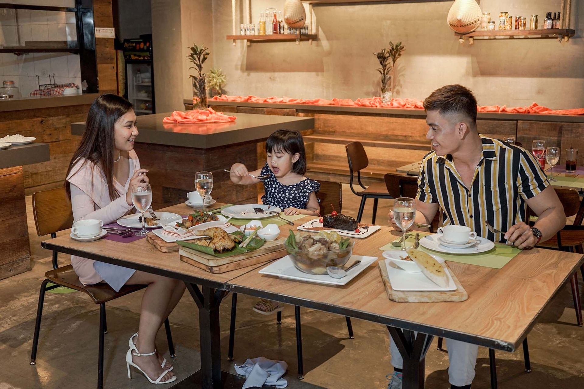 Family dining experience at hotel restaurant in Puerto Princesa with parents and child enjoying casual meal at wooden table.