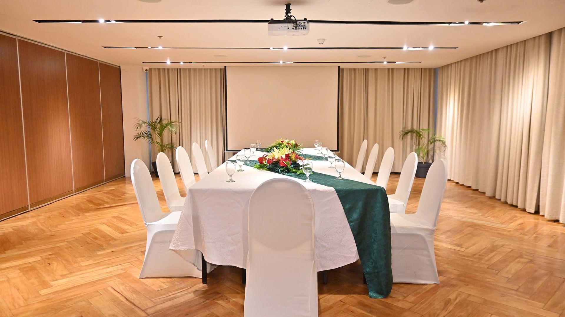 Elegant banquet room with a round table set for a meeting or dinner, surrounded by white-covered chairs.
