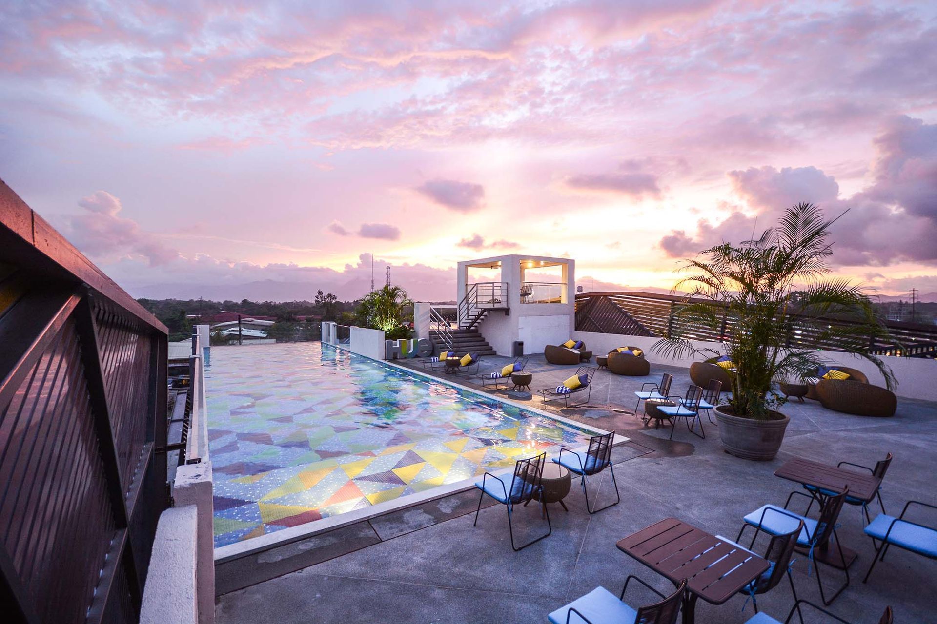 Outdoor terrace with colorful patterned floor, tables and chairs, and a pink sunset sky