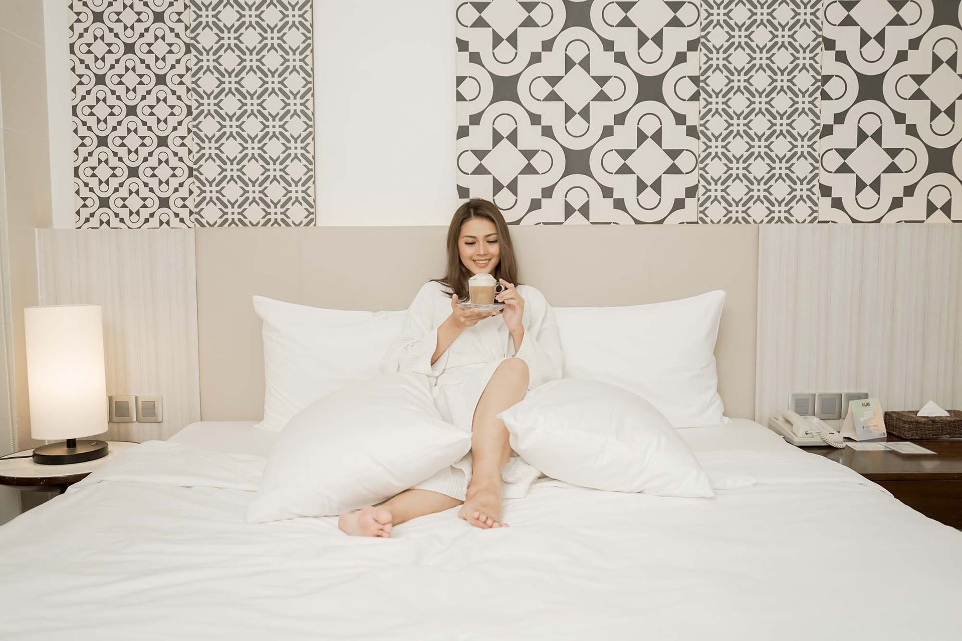Woman in white robe enjoying latte on bed at Hue Hotel Puerto Princesa