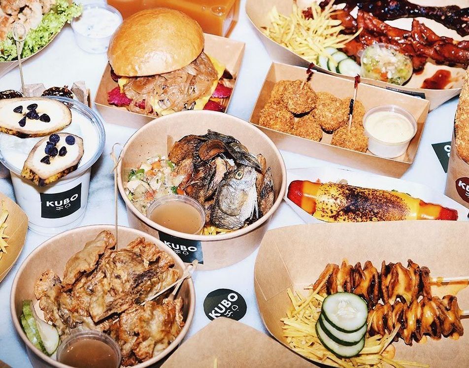A top-down view of various takeout containers filled with diverse Filipino food, including grilled skewers and rice bowls.