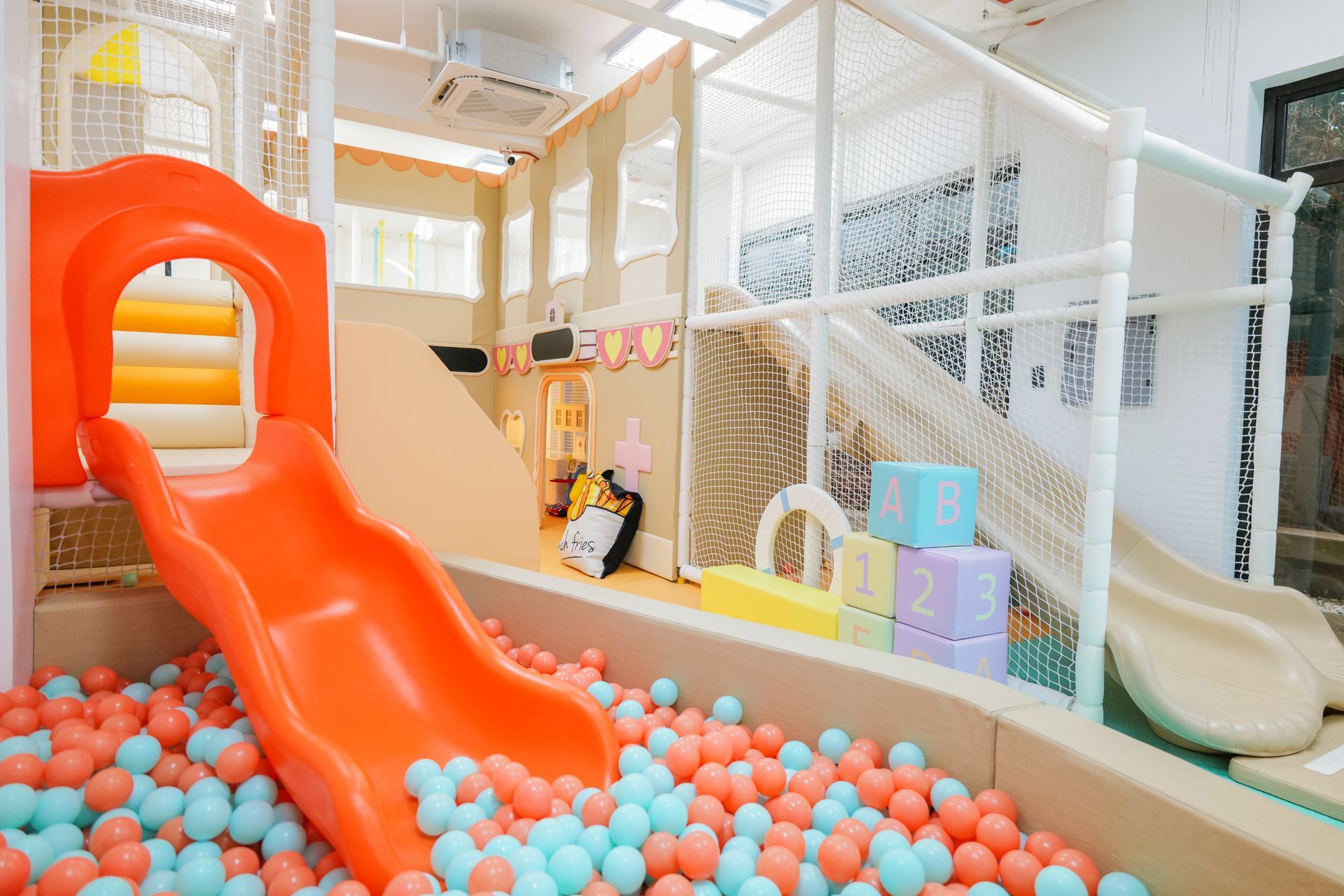 Indoor play area with bright orange slide, ball pit, and netted climbing structures