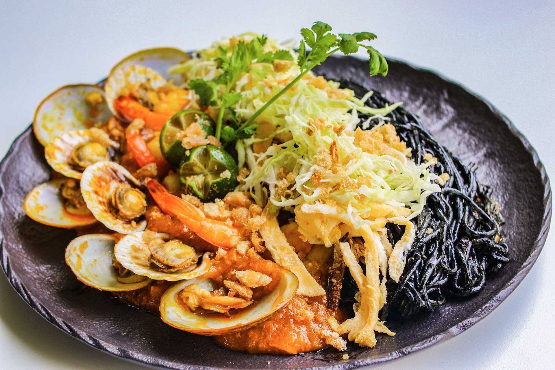 Seafood pasta with clams, shrimp, and black noodles on a black plate, garnished with greens