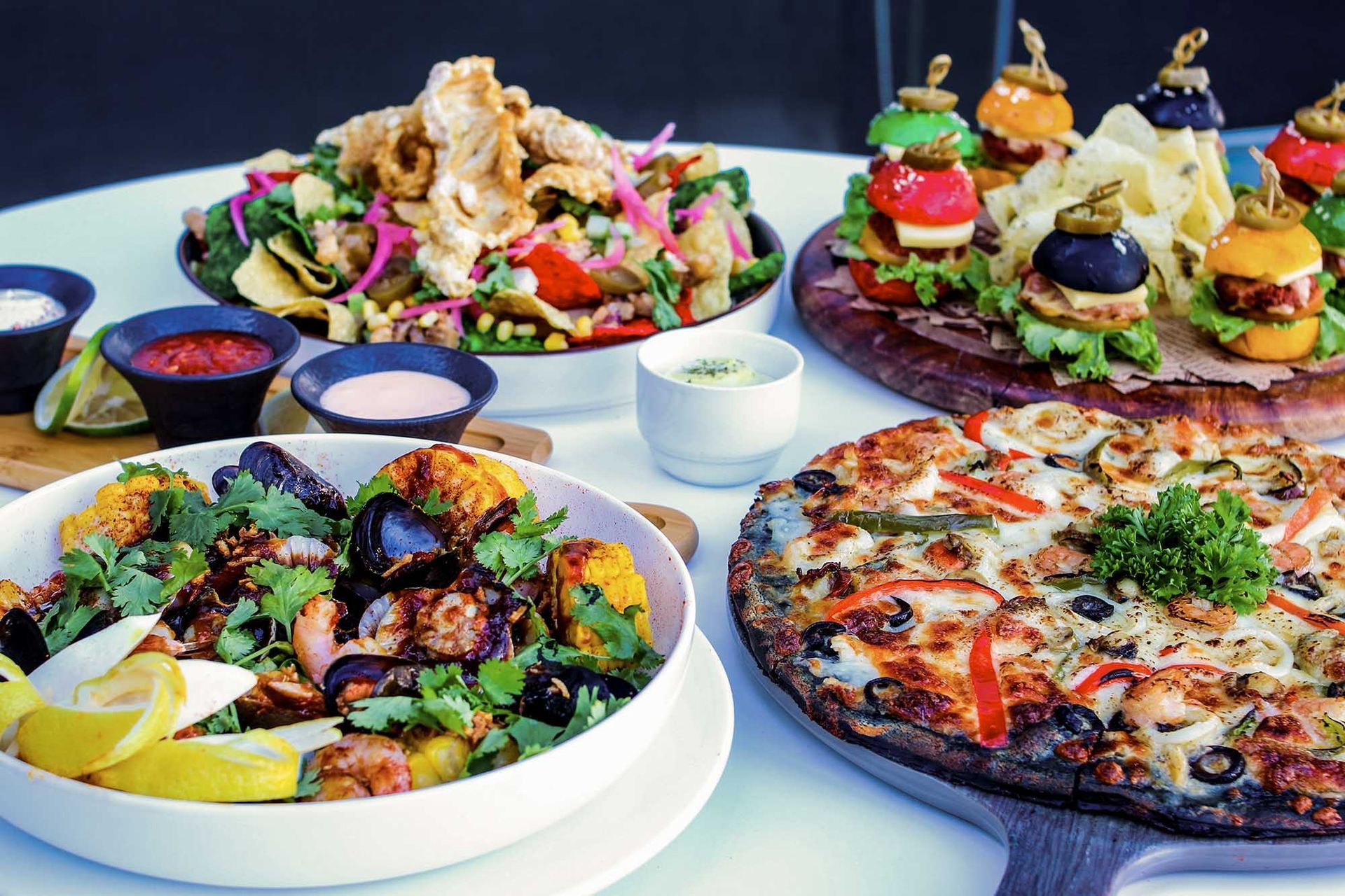 A table set with a variety of colorful dishes, including a salad, pizza, and sliders.