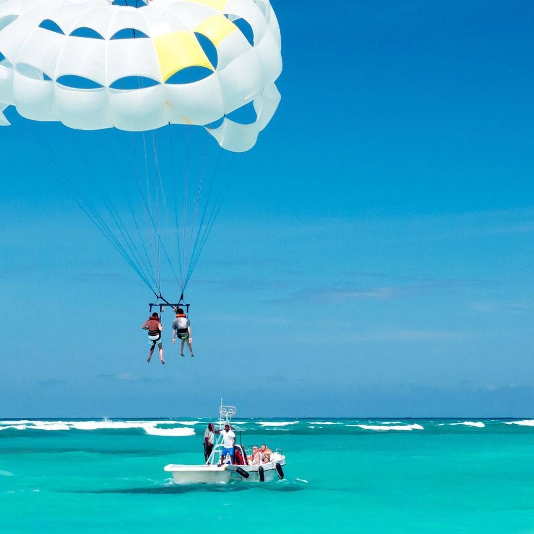 People parasailing over turquoise water, pulled by a boat on a sunny day.