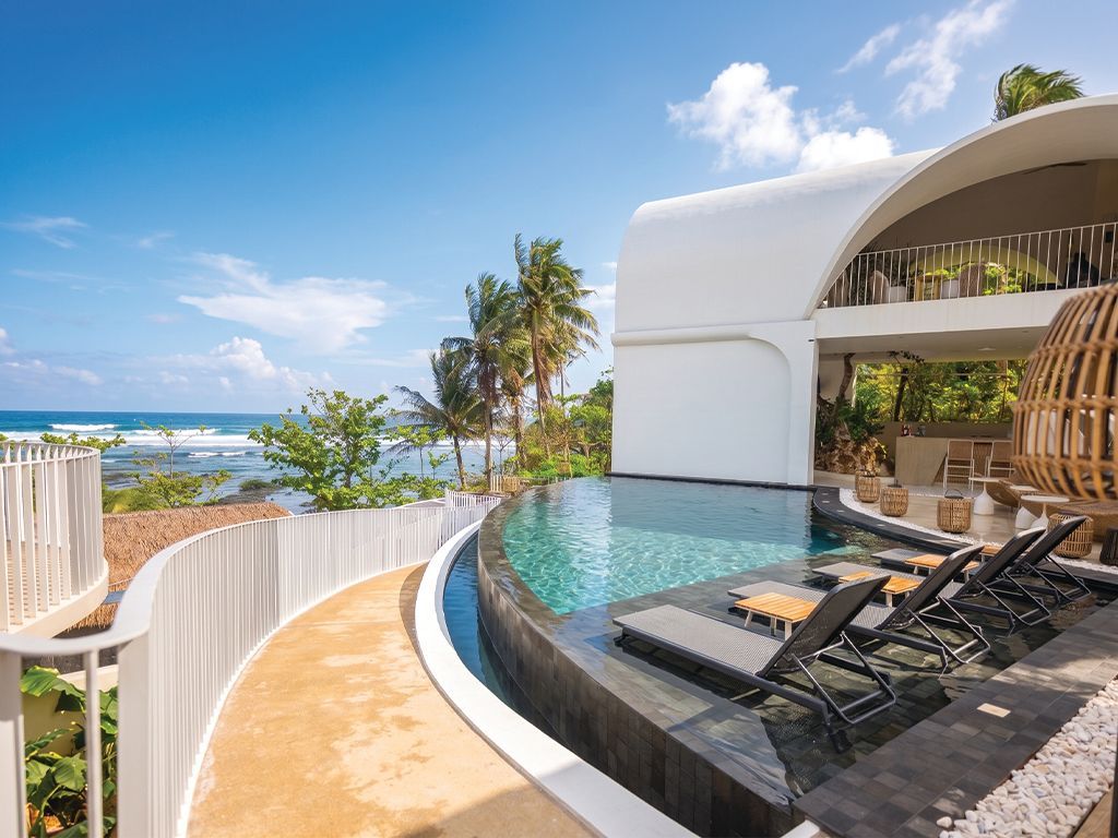Luxury infinity pool beside a white villa with lounge chairs and ocean views under a blue sky