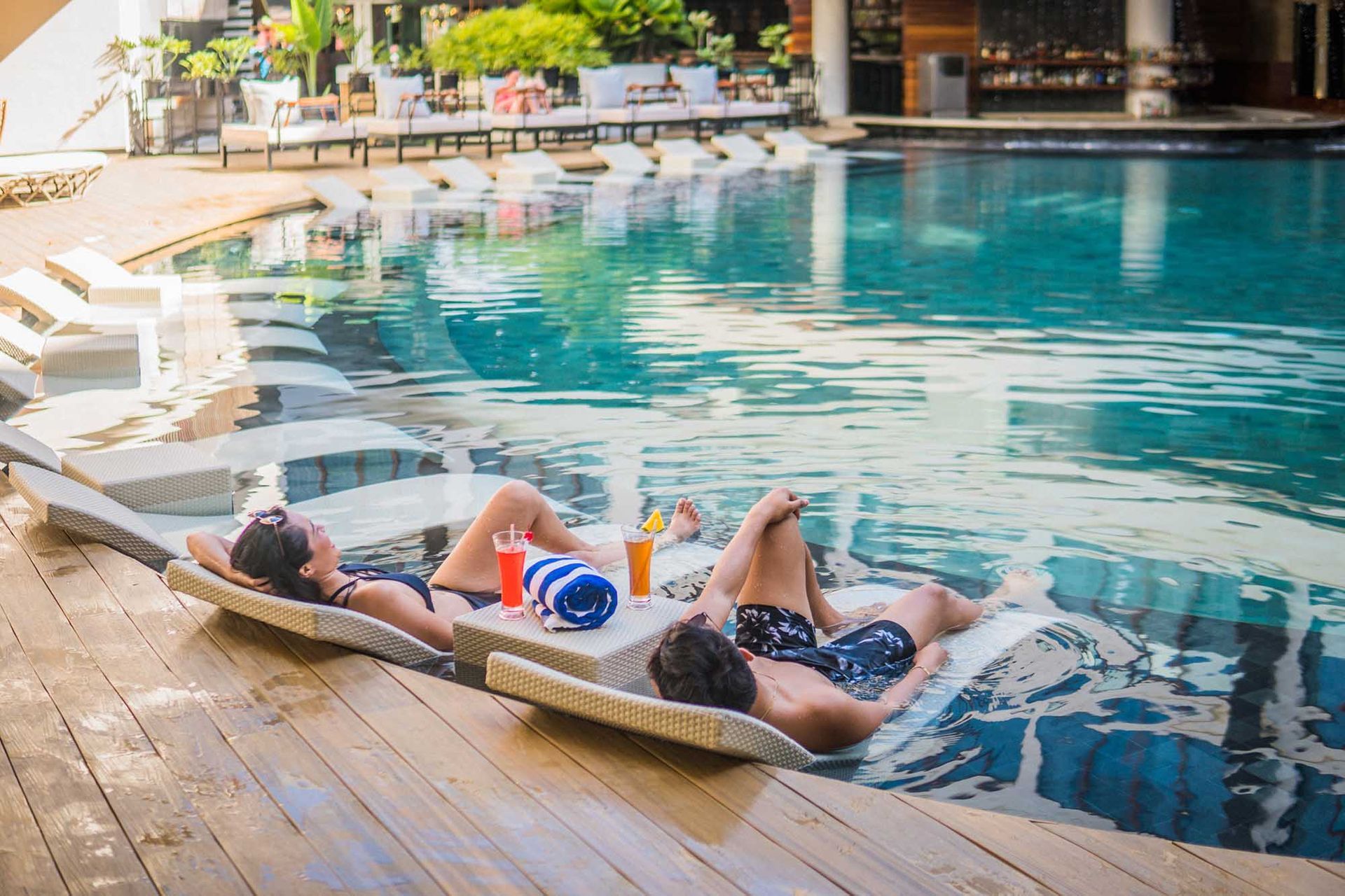 Couple relaxing in a pool on floating lounge chairs with drinks.