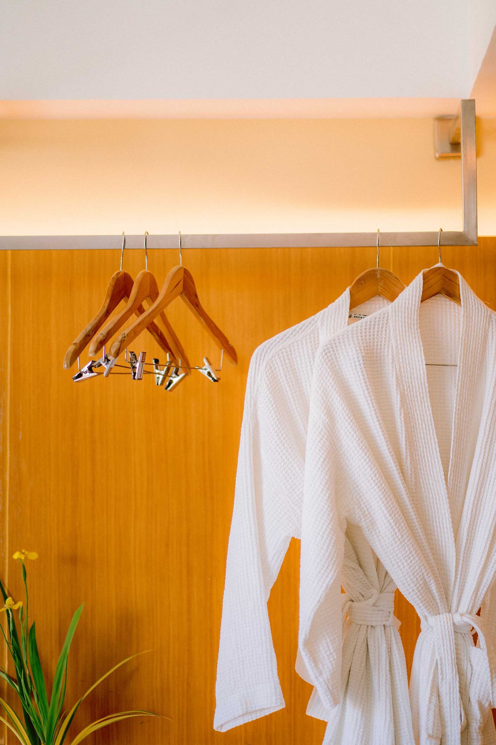 White waffle bathrobes hanging in wardrobe with wooden hangers against orange wall in Boracay hotel room