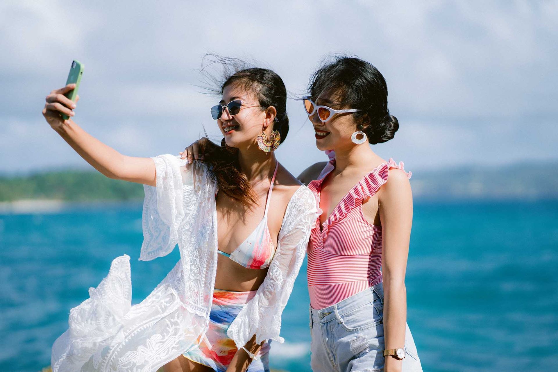 Two women in swimsuits taking a selfie by the ocean on a sunny day