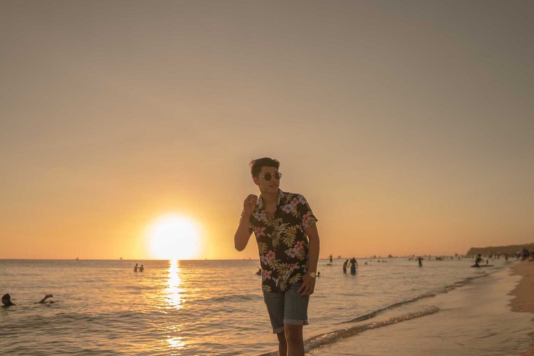 Man in floral shirt walks Boracay beach at golden sunset