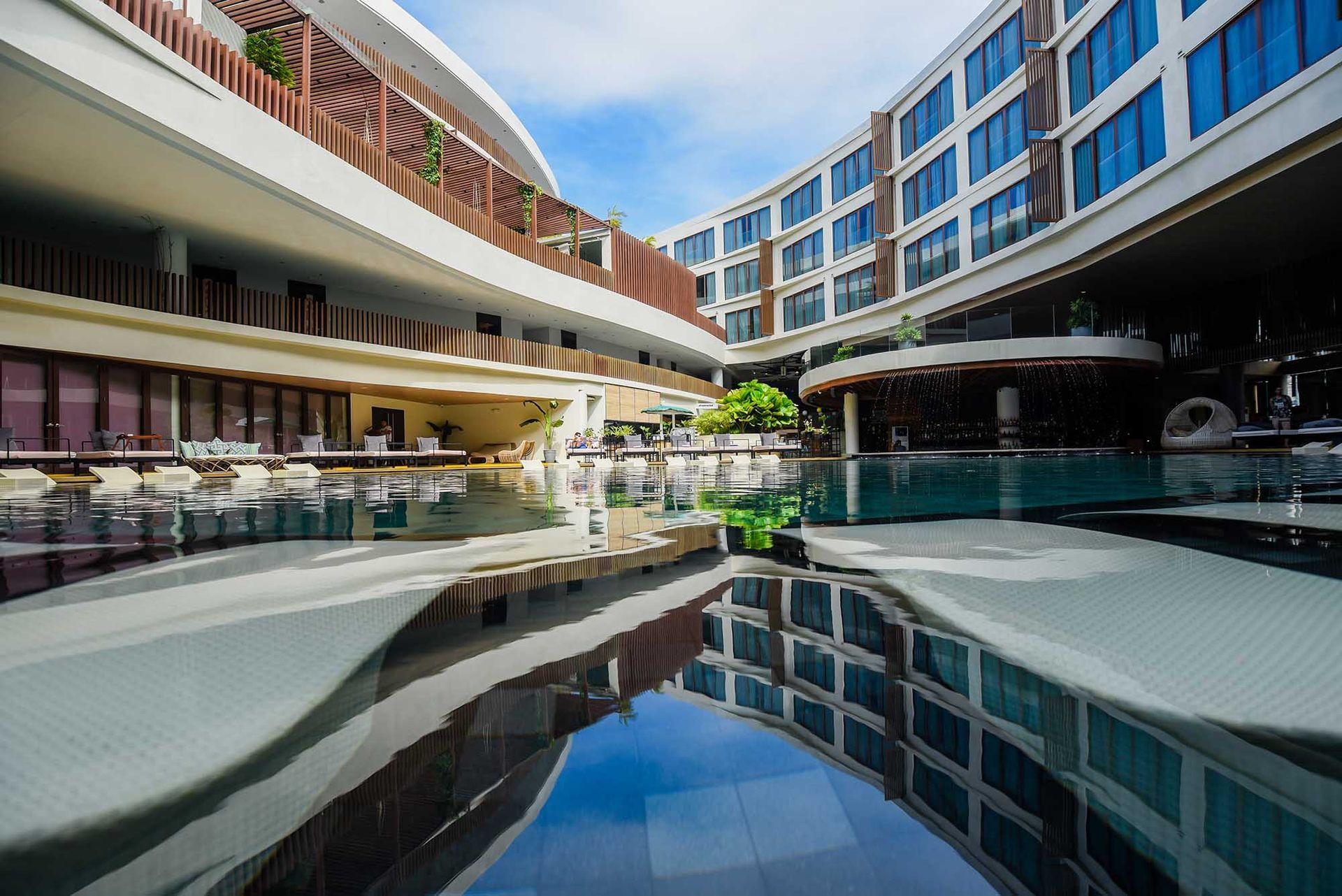 Modern hotel courtyard with pools, curved balconies, and glass reflections at dusk