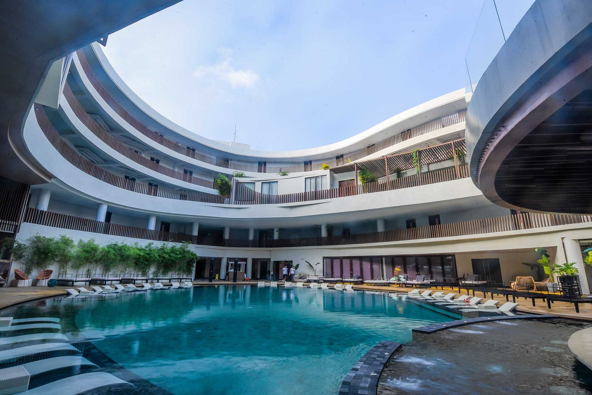 Modern hotel courtyard with a turquoise pool and curved multi-story balconies under a bright sky