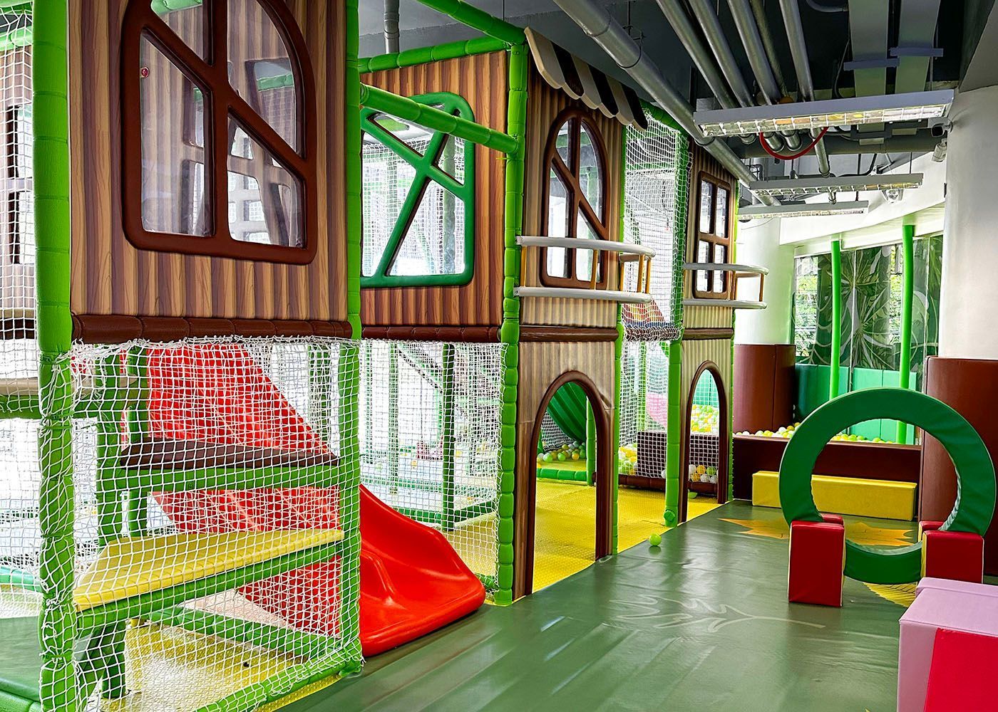 Colorful indoor play area with a slide, climbing nets, and green arch obstacles under a covered roof