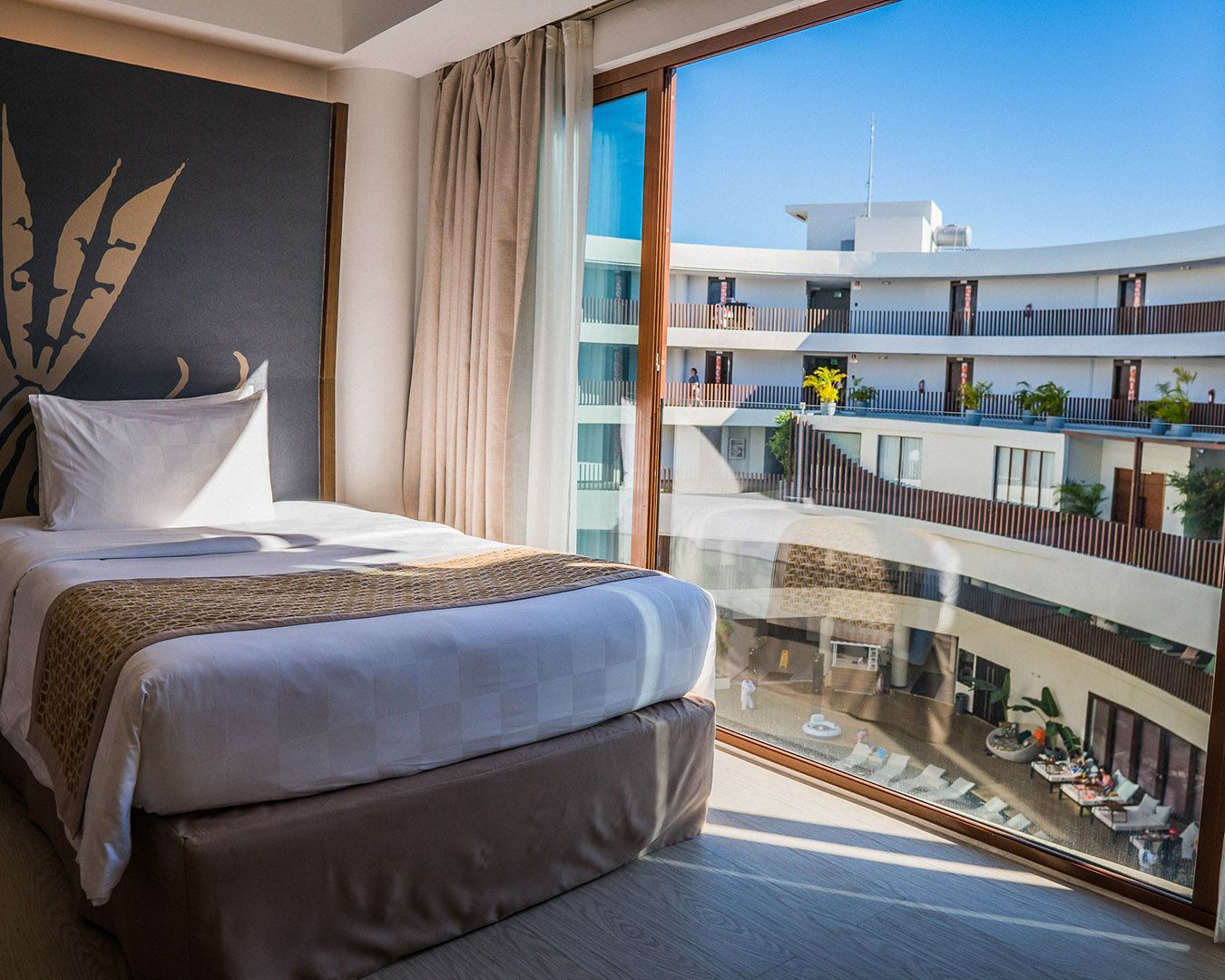 Hotel room with a bed and large window overlooking a bright oceanfront resort courtyard