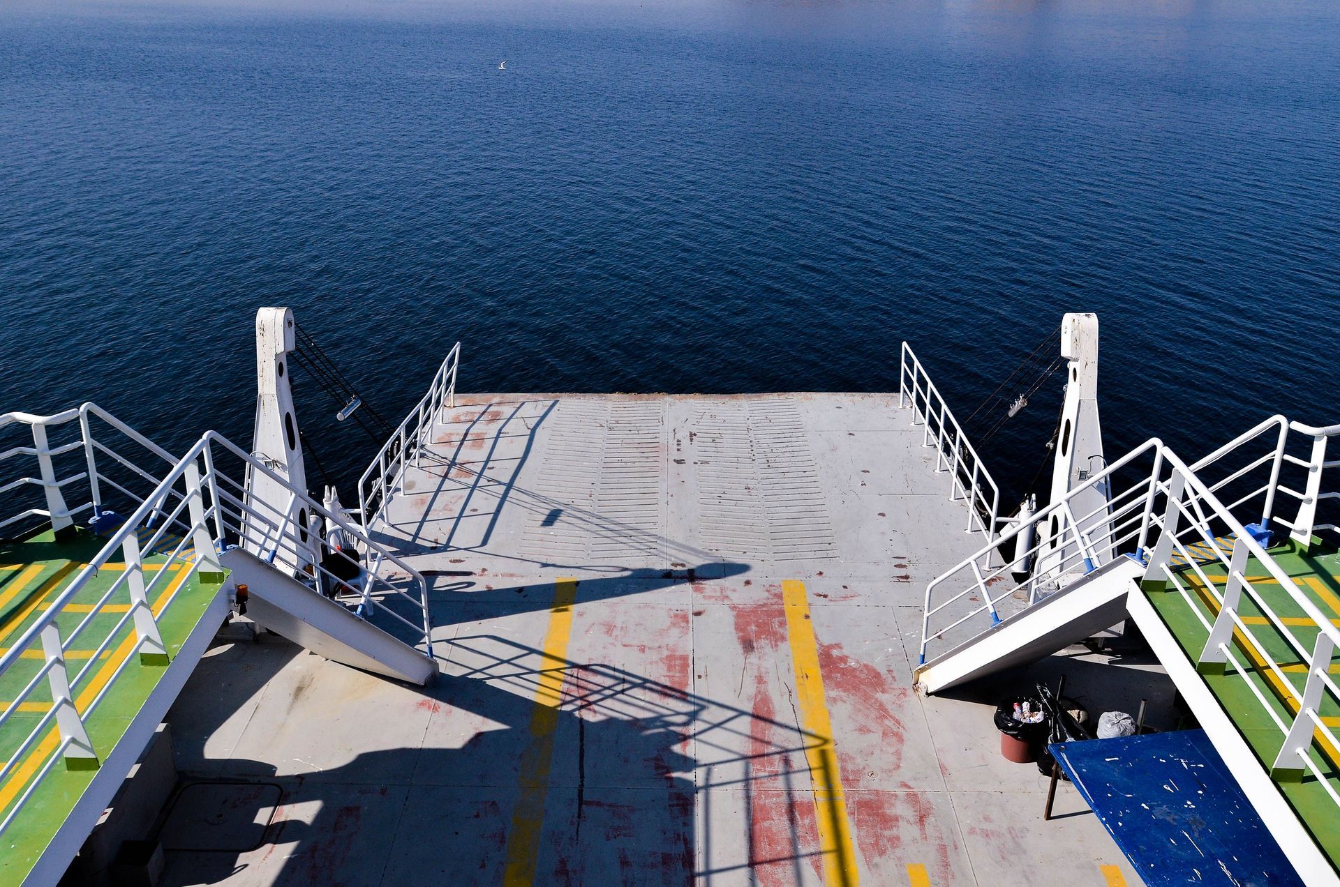 Ferry deck leading to open blue sea, with white railings and colorful painted markings.