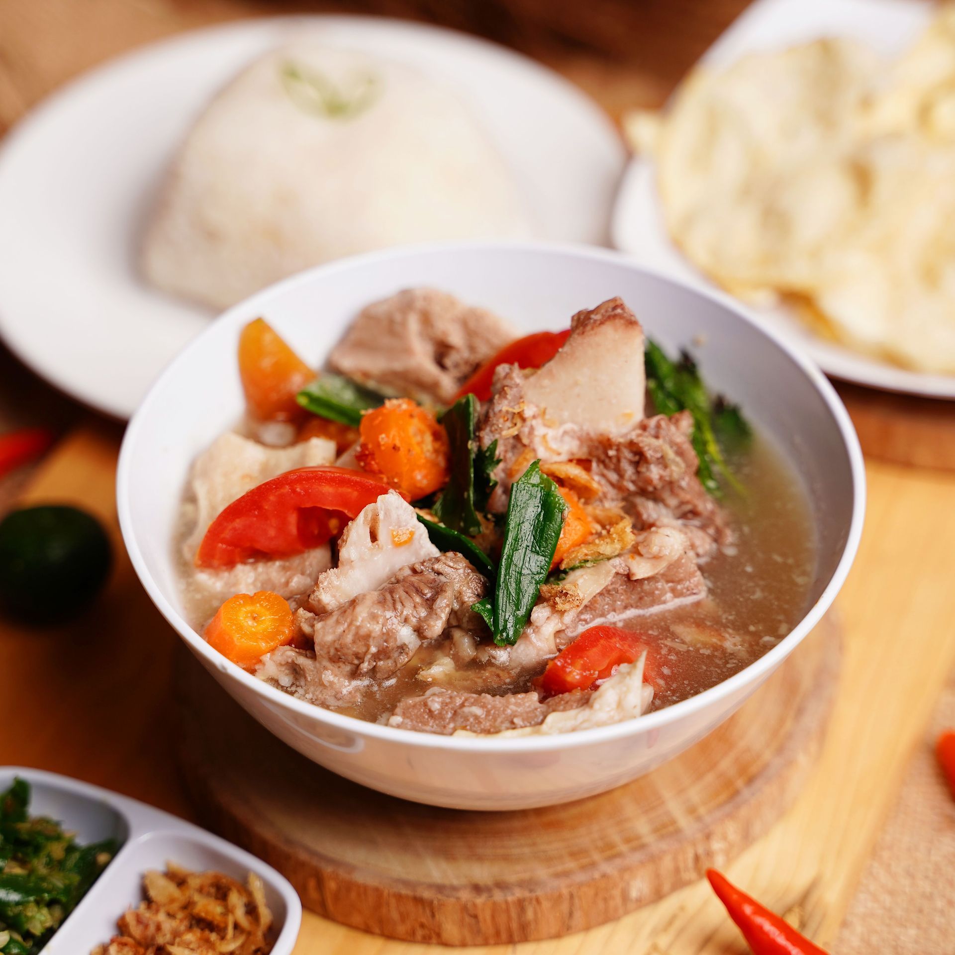 Bowl of beef soup with vegetables and rice, served with rice and crackers on the side