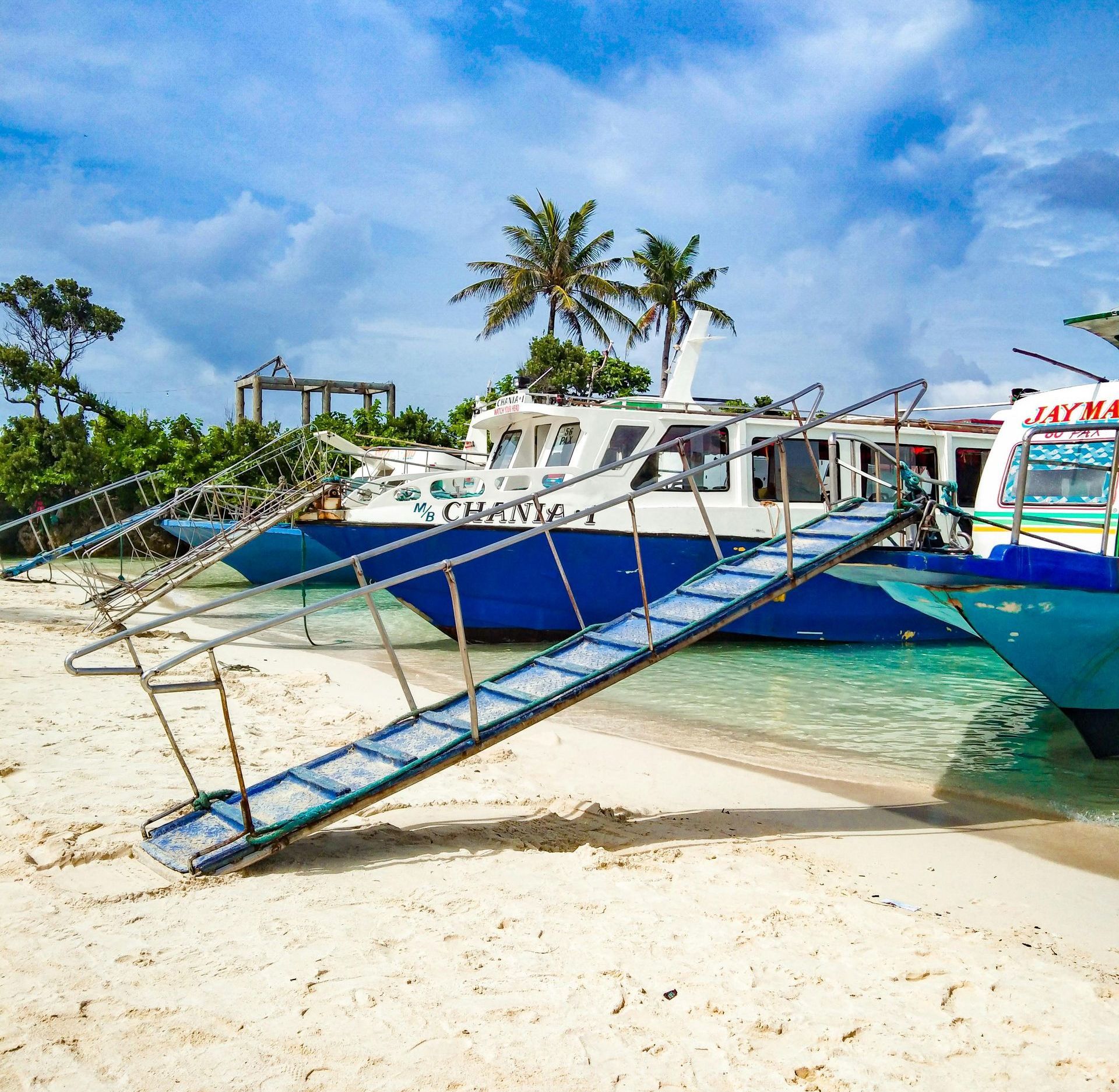 Blue-and-white boat on a sandy tropical beach with palm trees and a bright sky