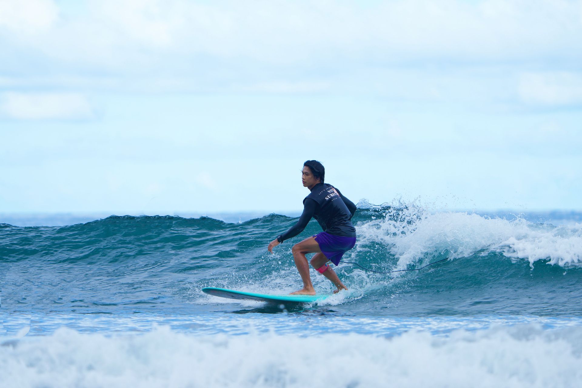 Surfer in a blue wetsuit riding a wave in the ocean under a bright sky