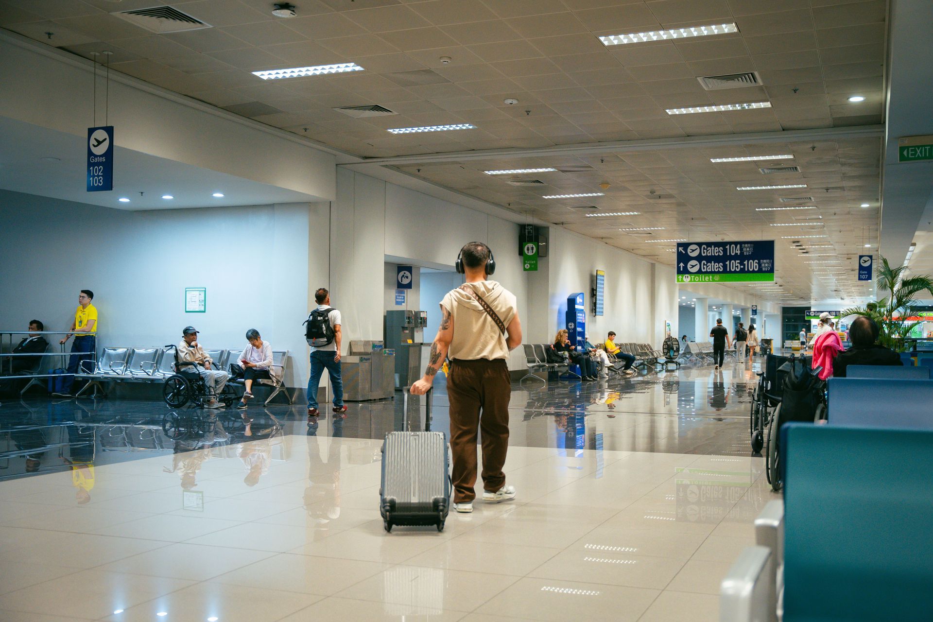 Traveler pulling suitcase through bright airport terminal with seated passengers in the background
