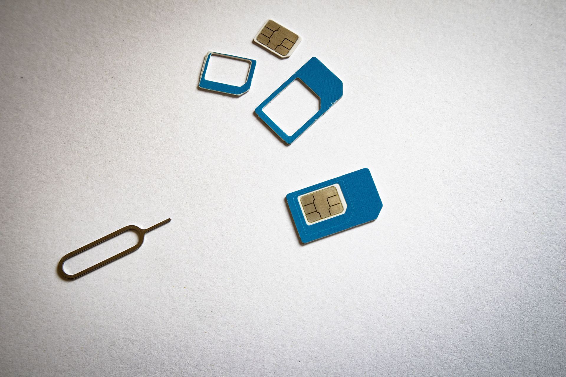SIM card tray tool and several blue SIM card adapters on a white surface