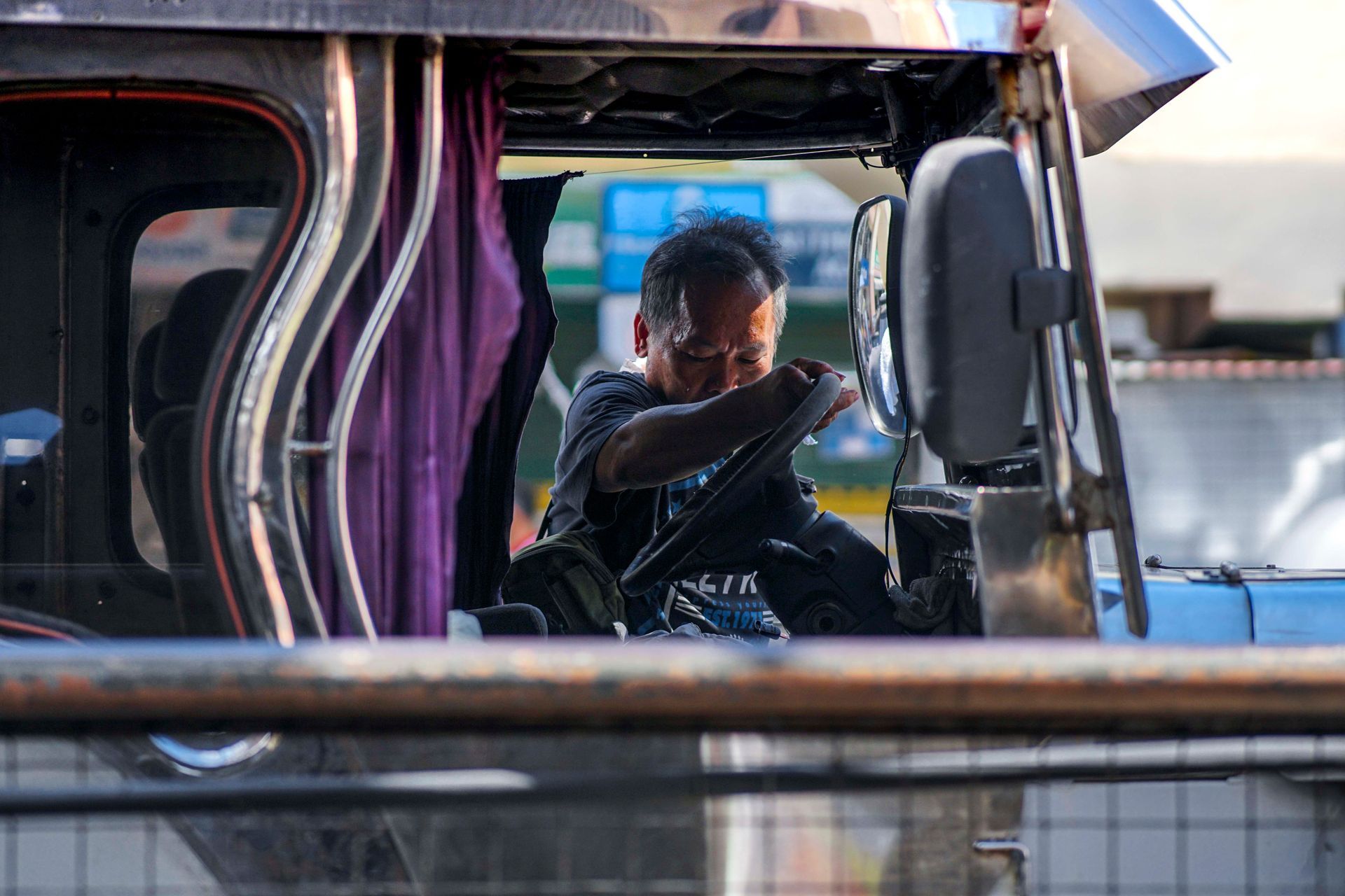Man looking out from a decorated vehicle cab, with purple curtains and a blue side mirror.