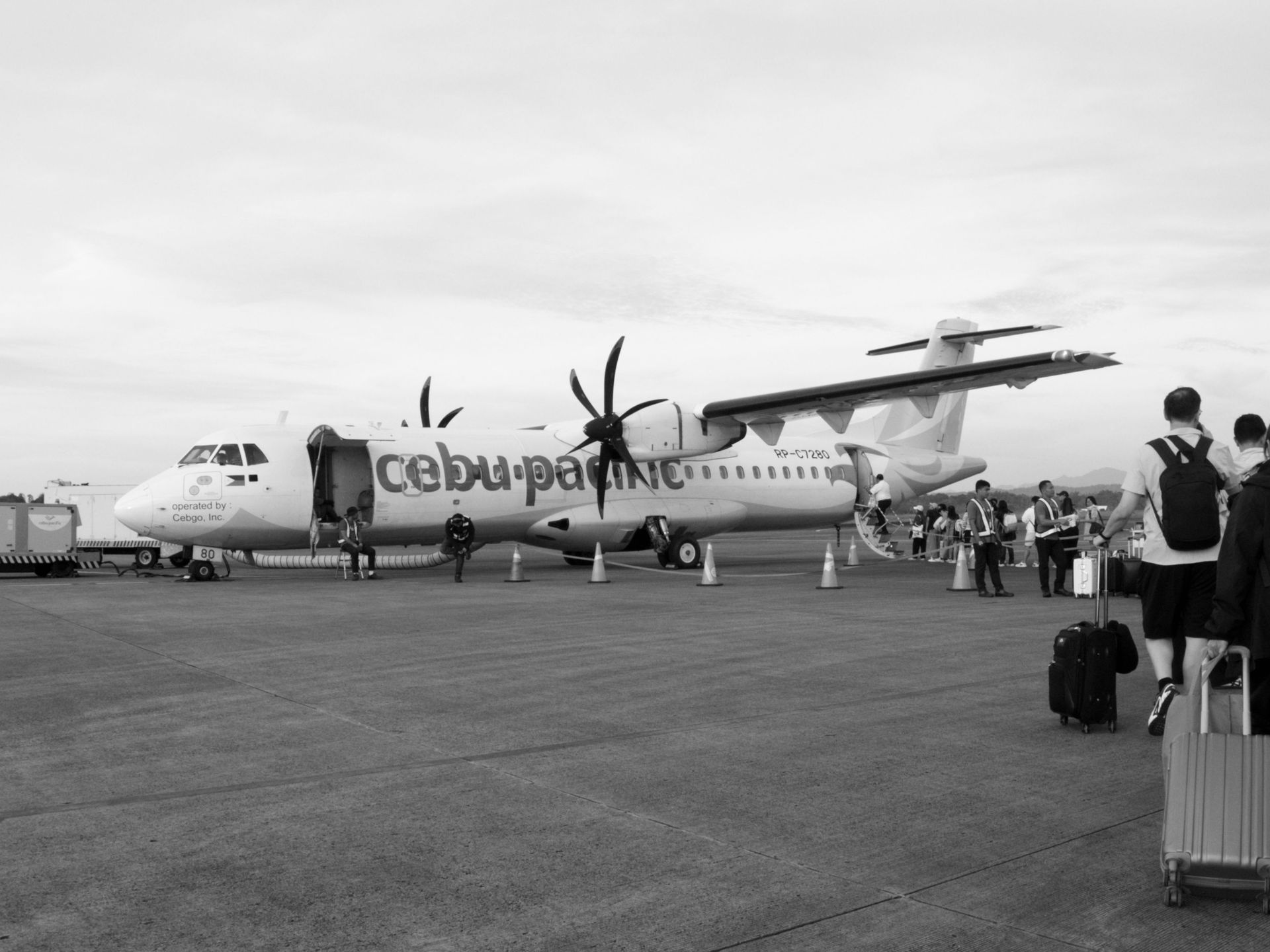 Cebu Pacific turboprop plane on the tarmac with passengers boarding under overcast skies